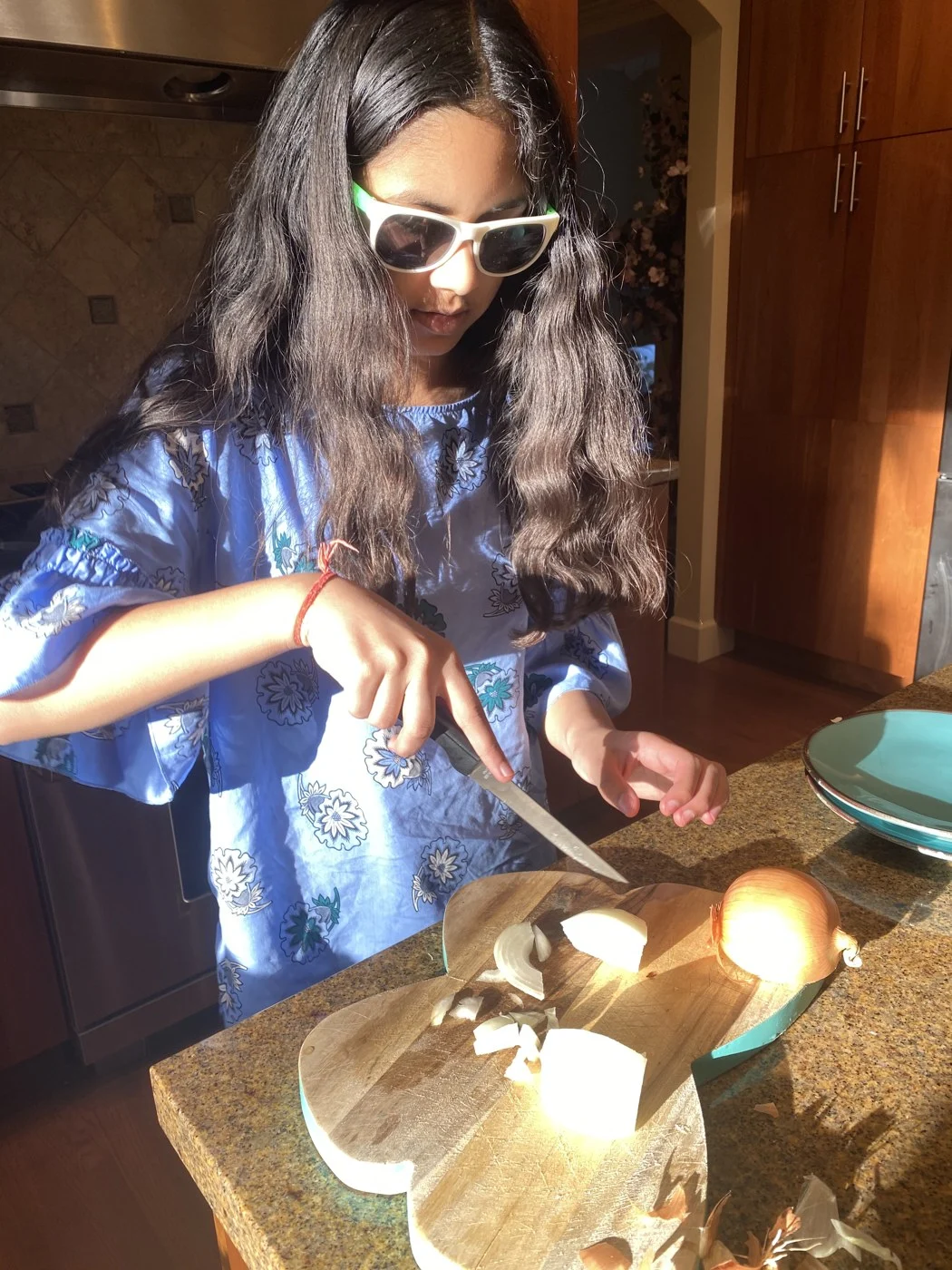Chopping an onion while wearing sunglasses in the kitchen.