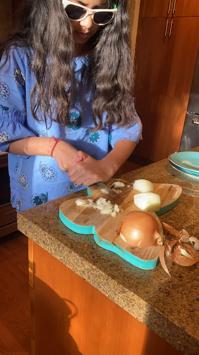 Dicing onions on a wooden board while wearing sunglasses.