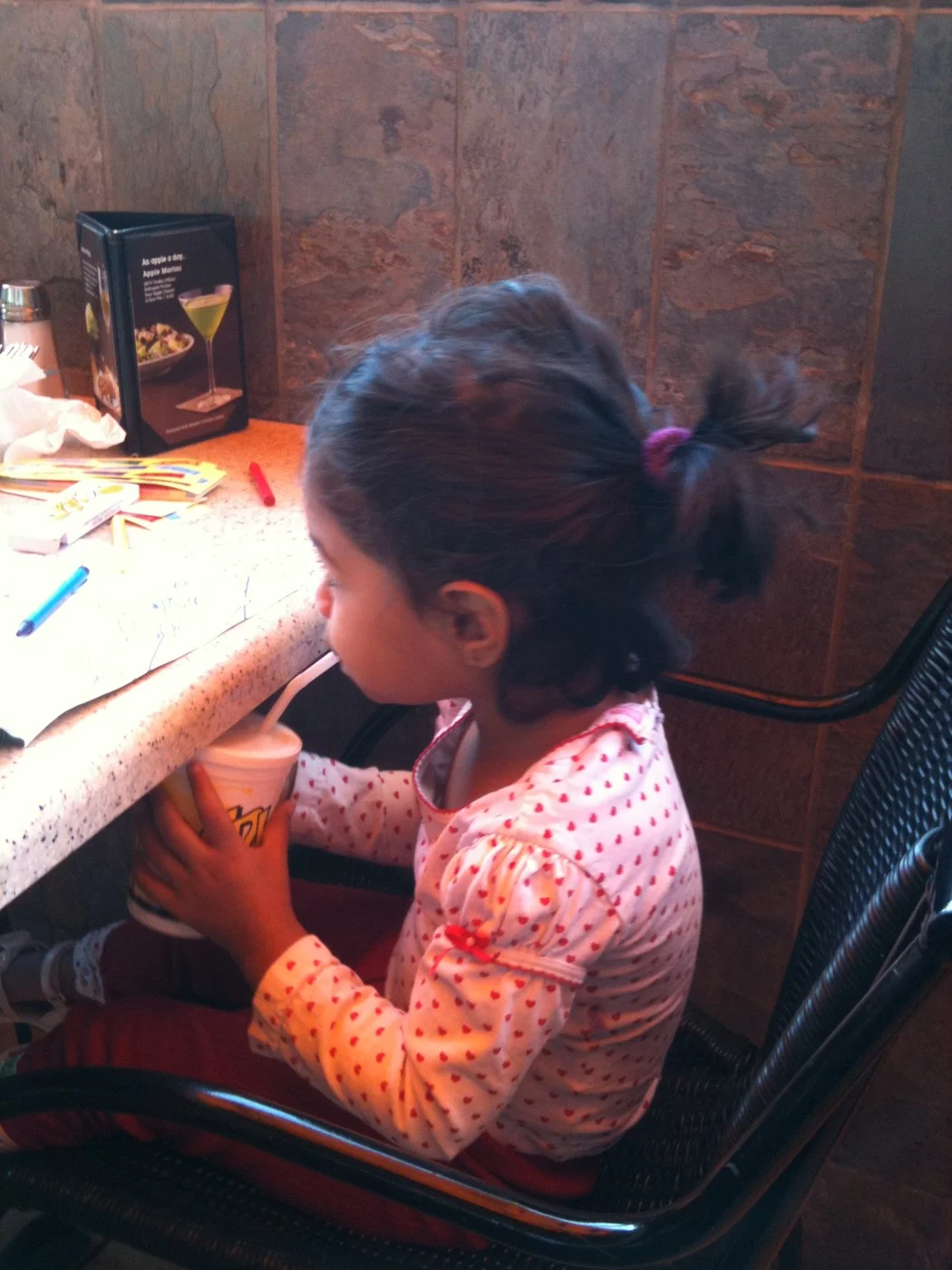 A young child holding a drink while sitting at a restaurant counter.
