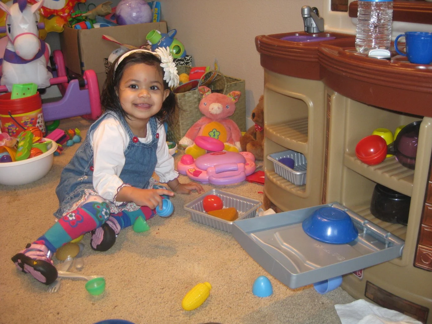 A young child playing beside a toy kitchen and toy food.