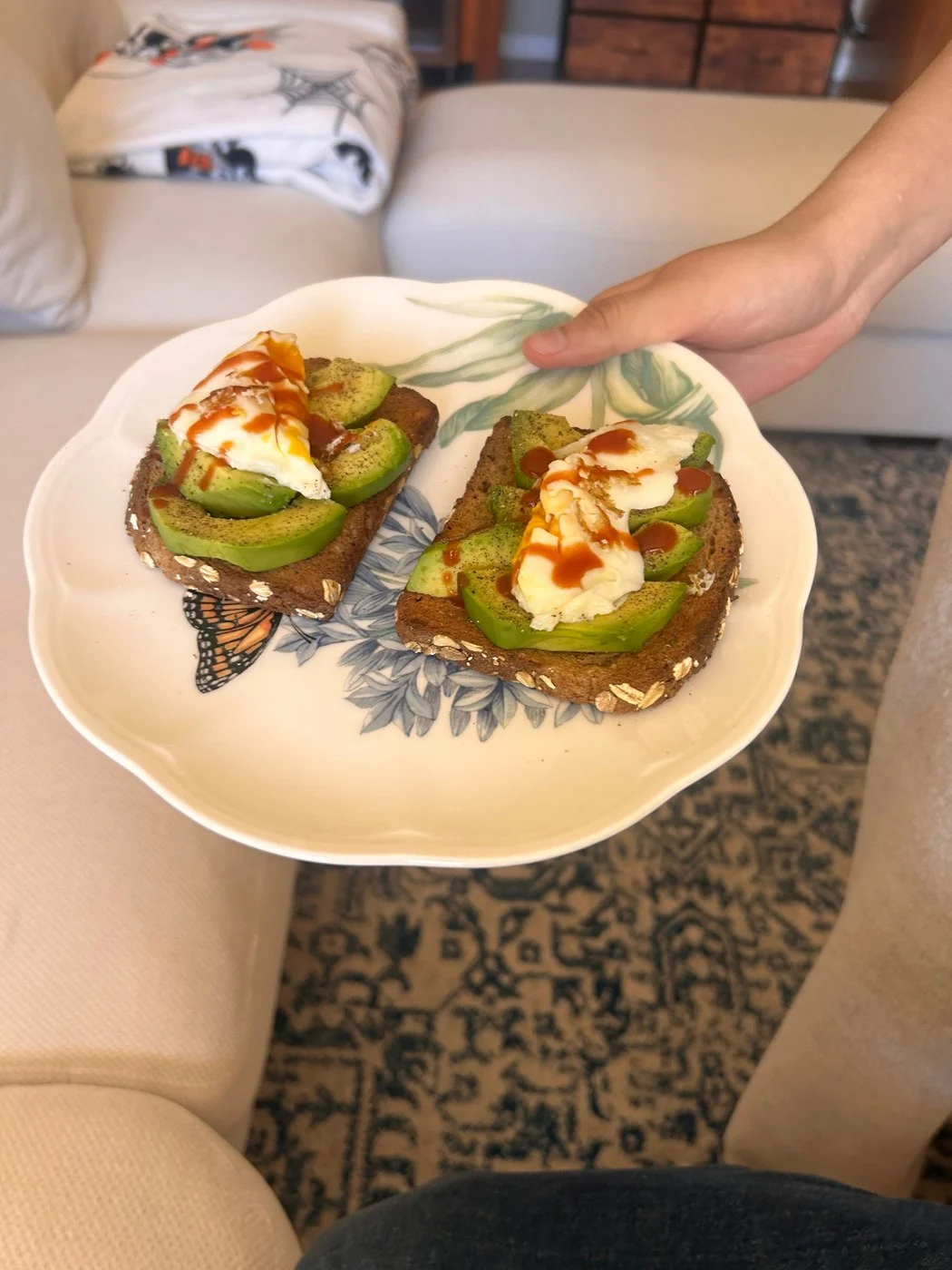 Two avocado toasts topped with eggs and streaks of red sauce.