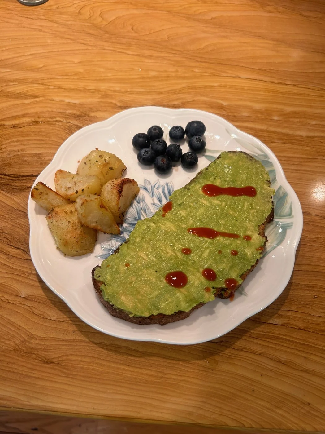 Avocado-topped toast served with blueberries and browned potato pieces.