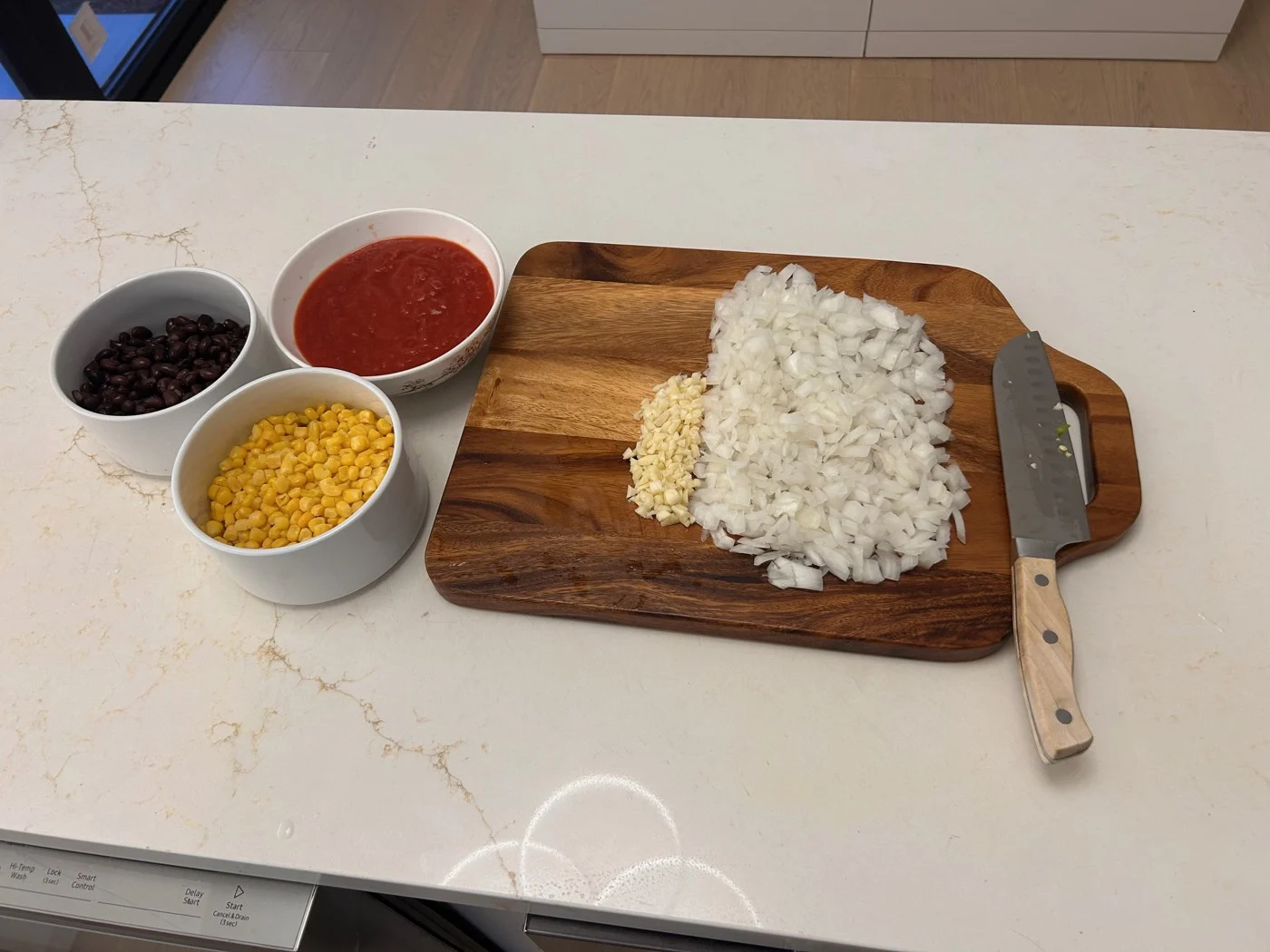 Bowls of dark beans, corn and tomato sauce beside chopped onion and garlic.