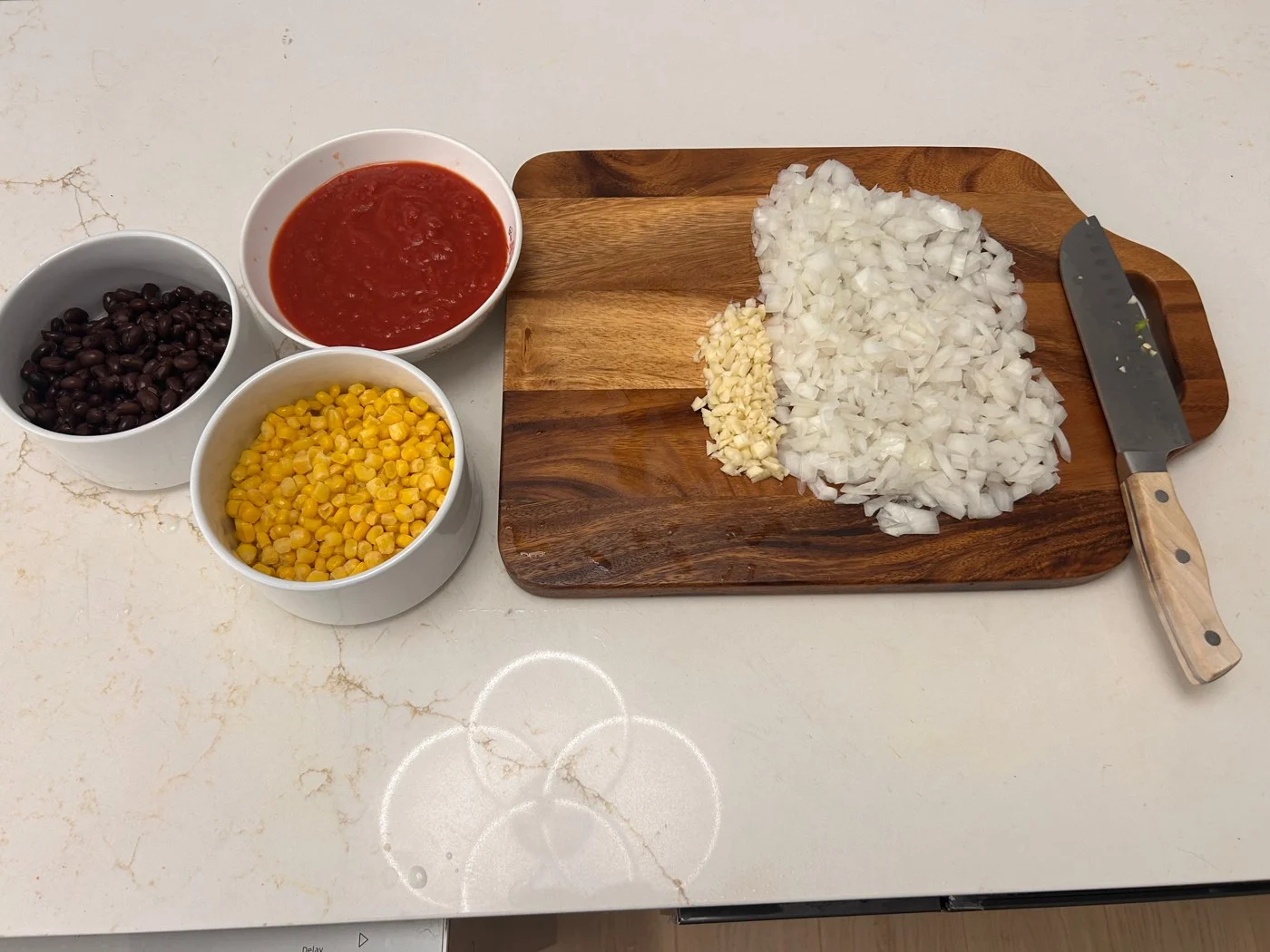 Chili ingredients arranged around a board of finely chopped onion and garlic.