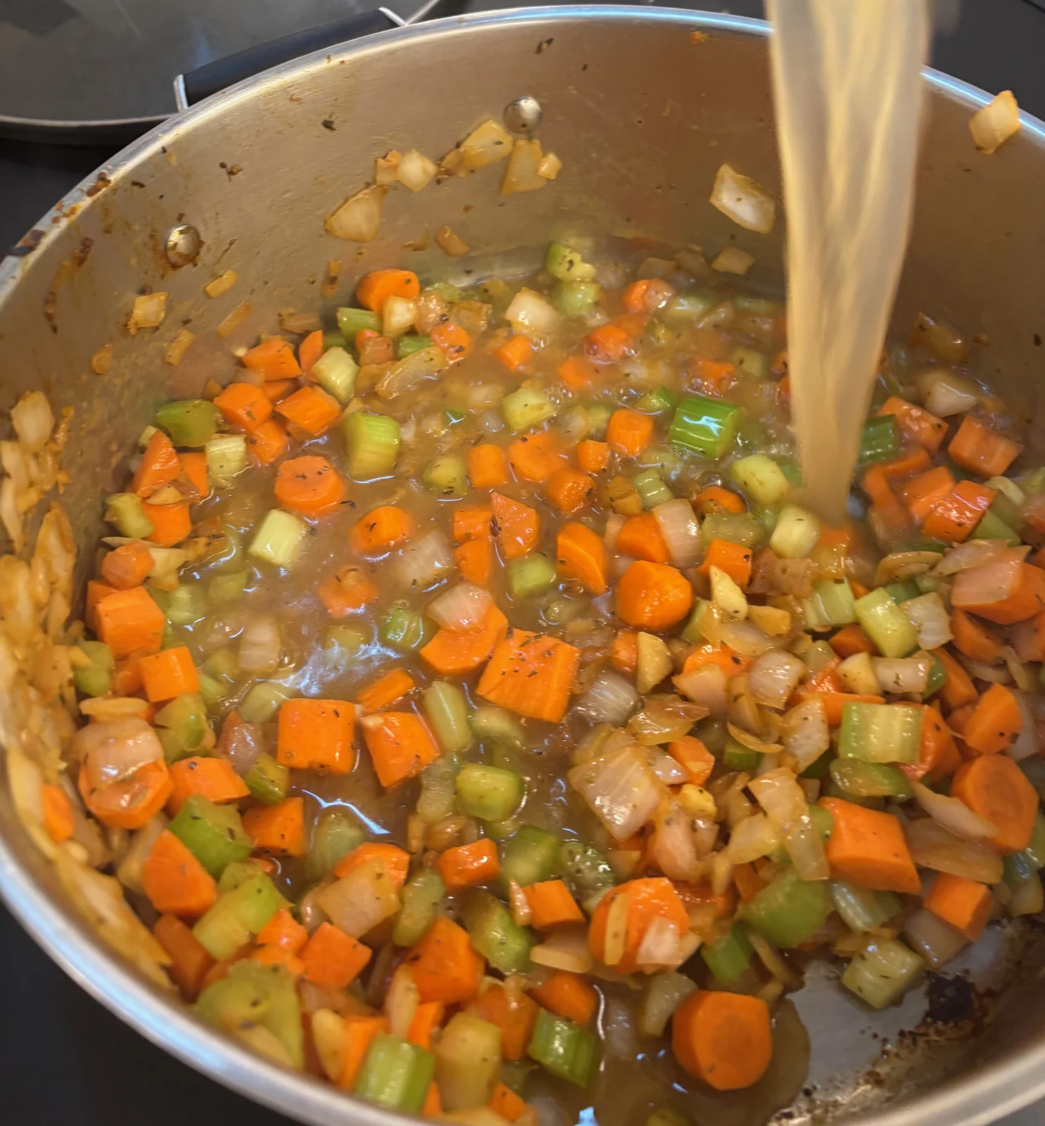Carrot, celery and onion chunks in a pot while light-colored liquid is poured in.
