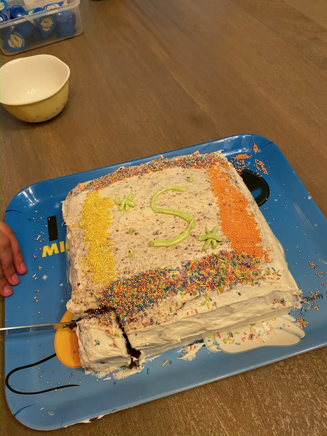 A pale-frosted sheet cake decorated with colorful sprinkles and a green piped letter.