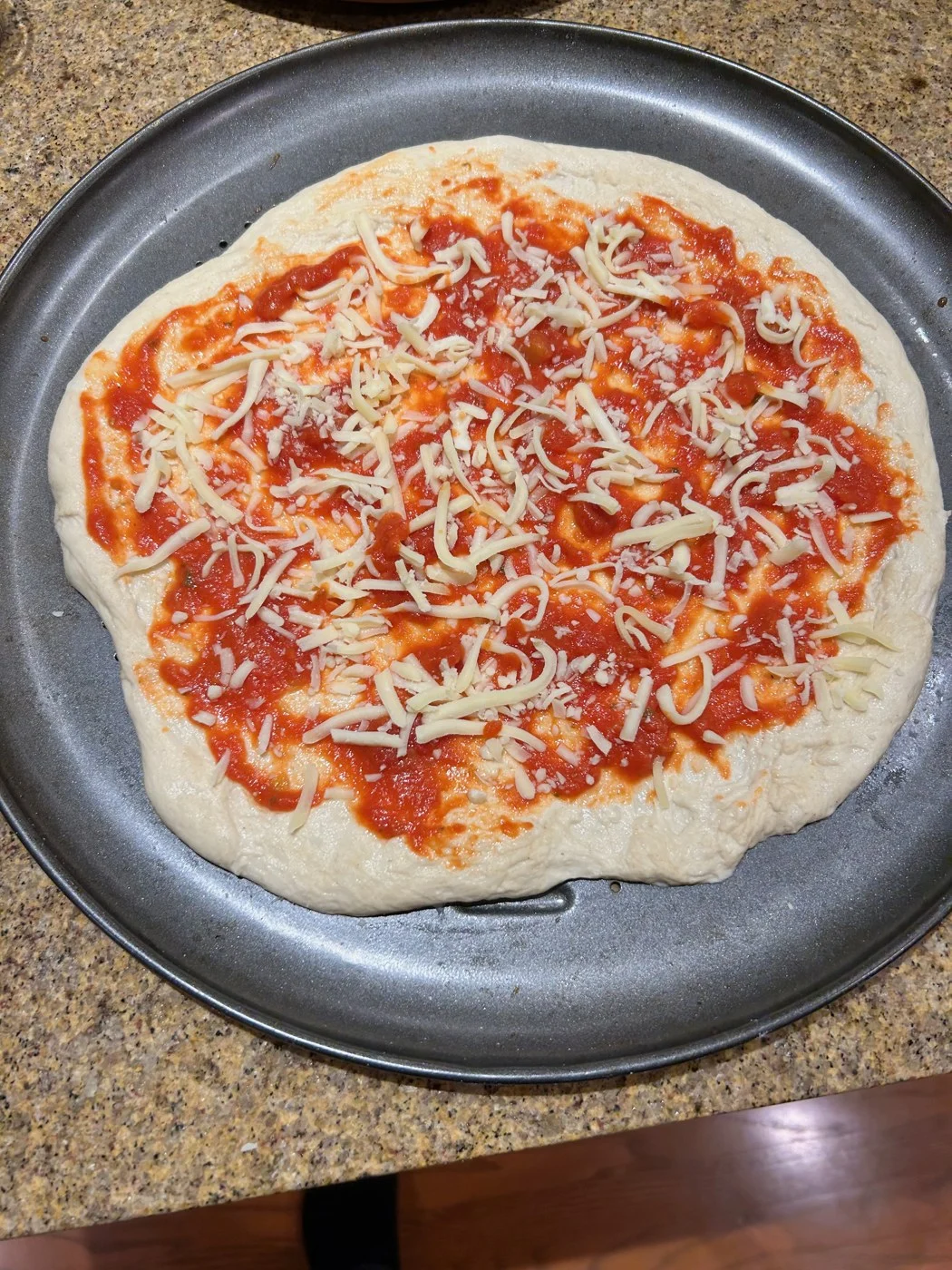 Unbaked pizza dough topped with tomato sauce and shredded cheese.