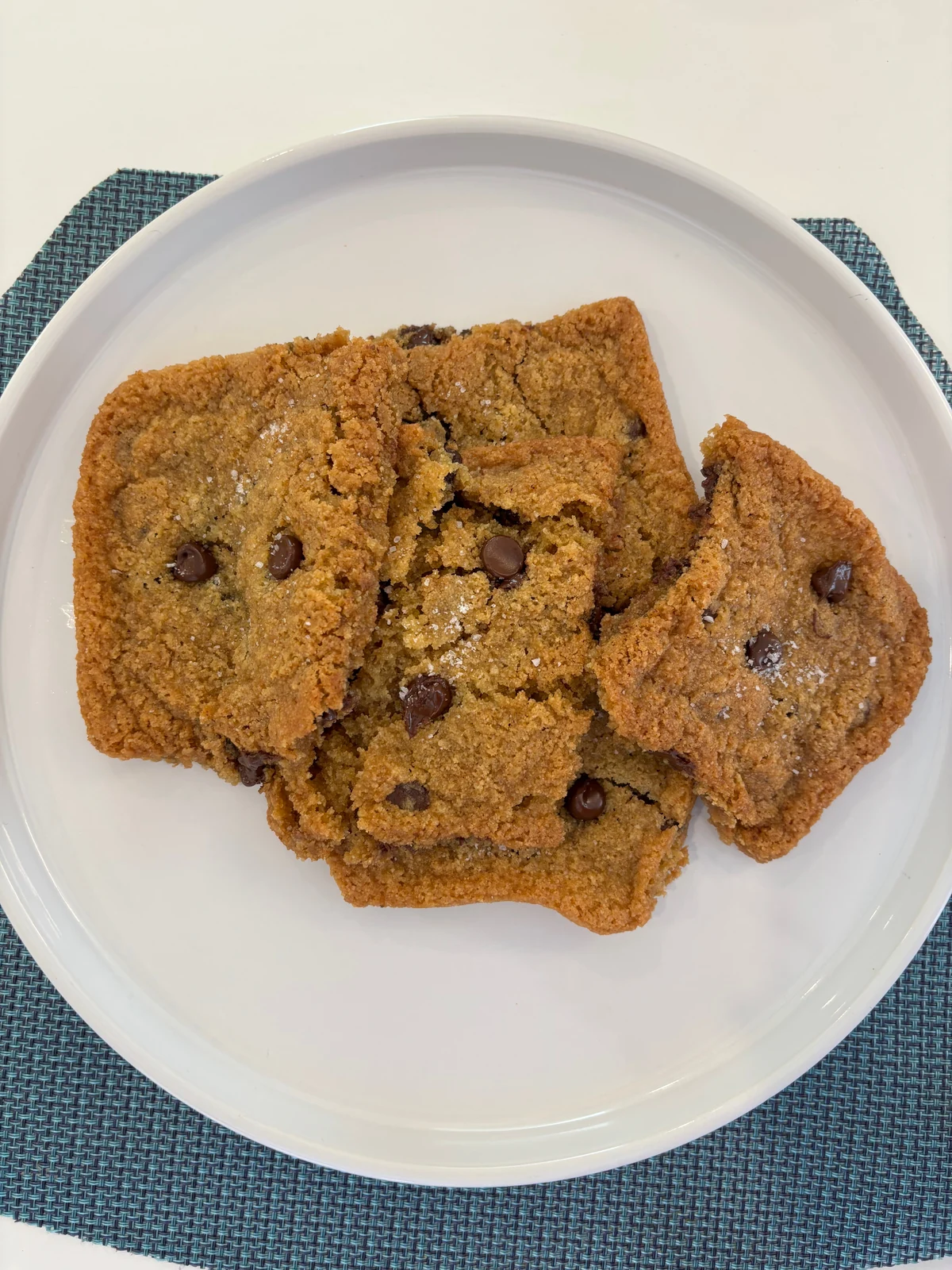 Thin golden square/irregular broken pieces with spread-cookie edges, chocolate chips and white granules on top.
