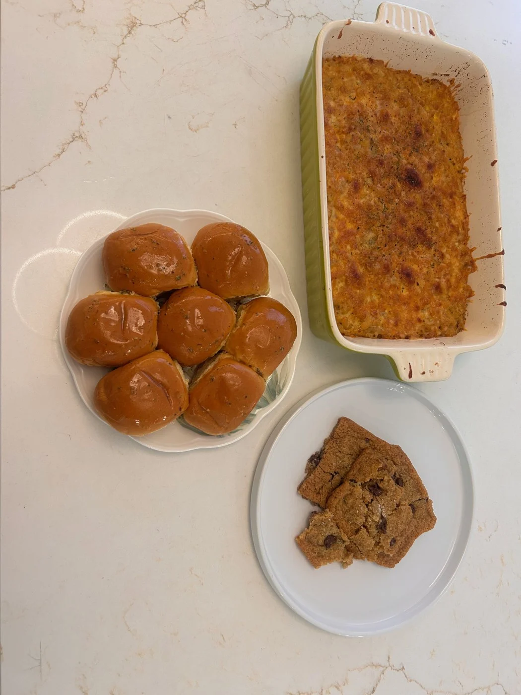 Baked macaroni in a casserole dish beside a plate of rolls and cookie pieces.