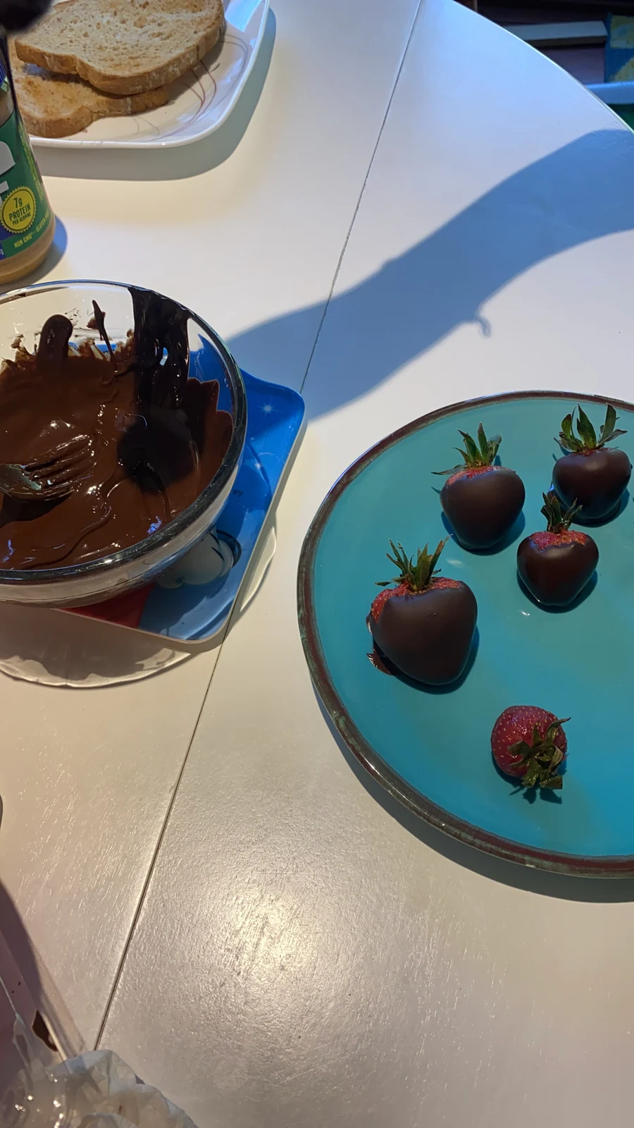 Several whole strawberries dipped in chocolate on a teal plate; melted chocolate bowl nearby.