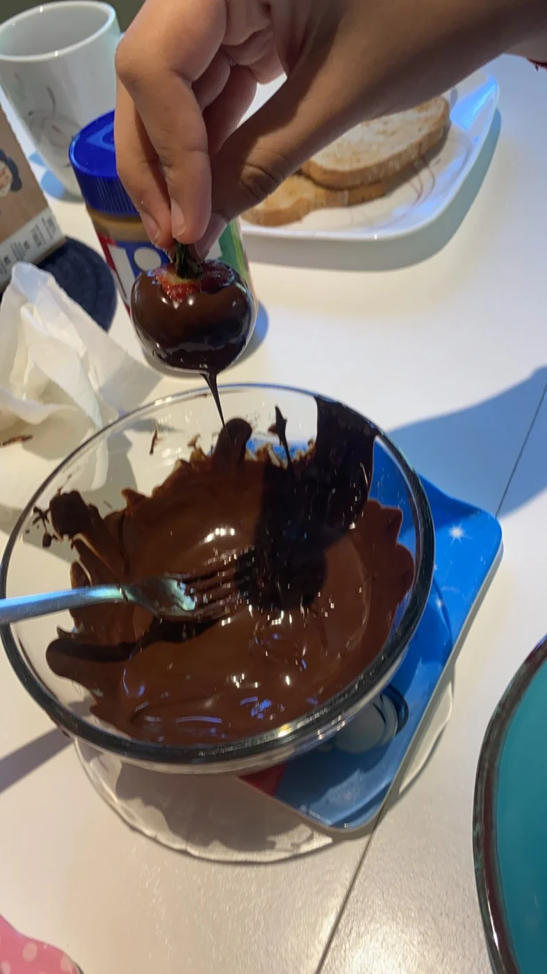 Dipping a whole strawberry into a bowl of melted chocolate.