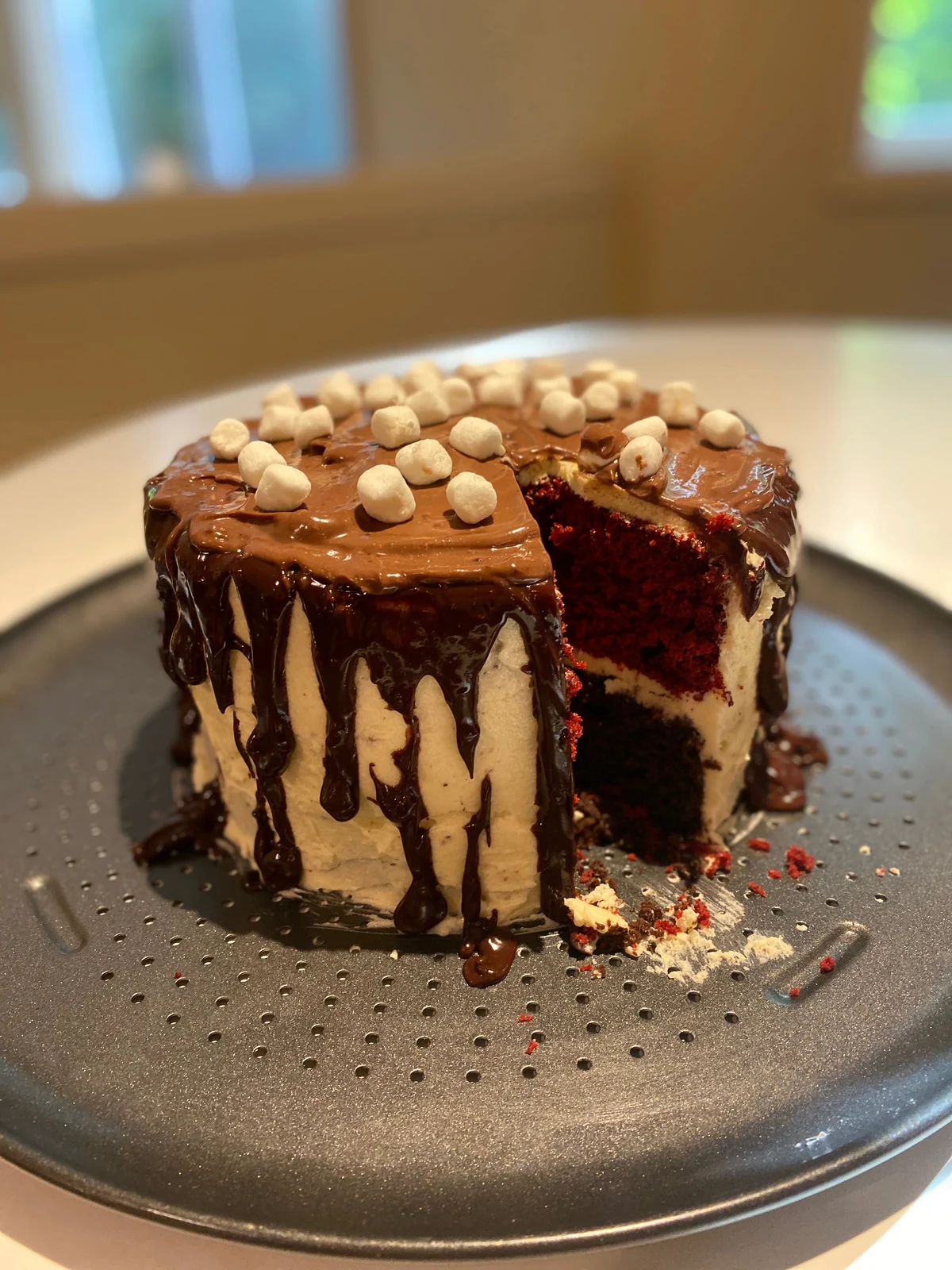 A wedge cut from the marshmallow drip cake reveals distinct red and dark chocolate-colored layers.