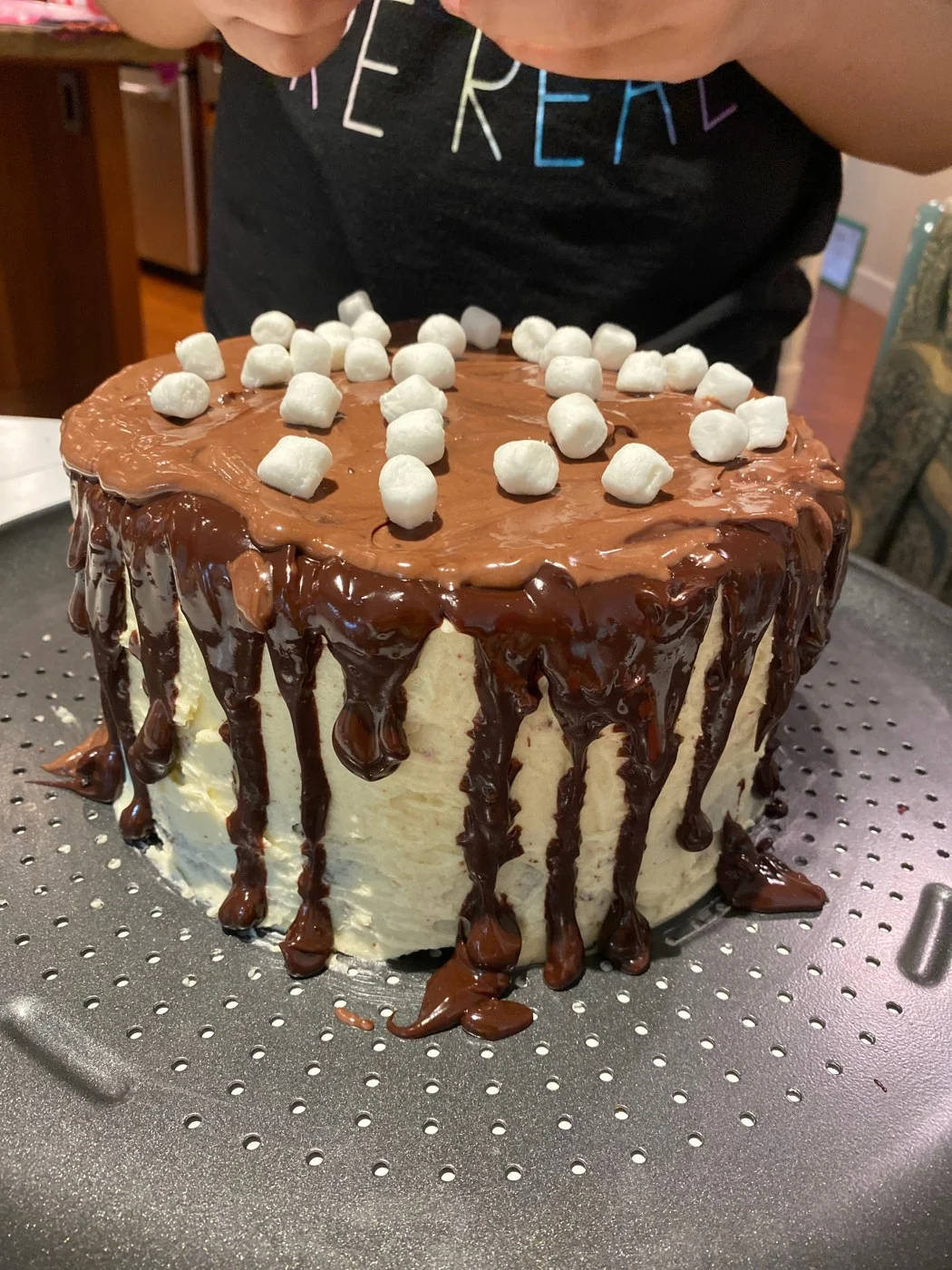 Adding small white marshmallows to a chocolate-drip cake.