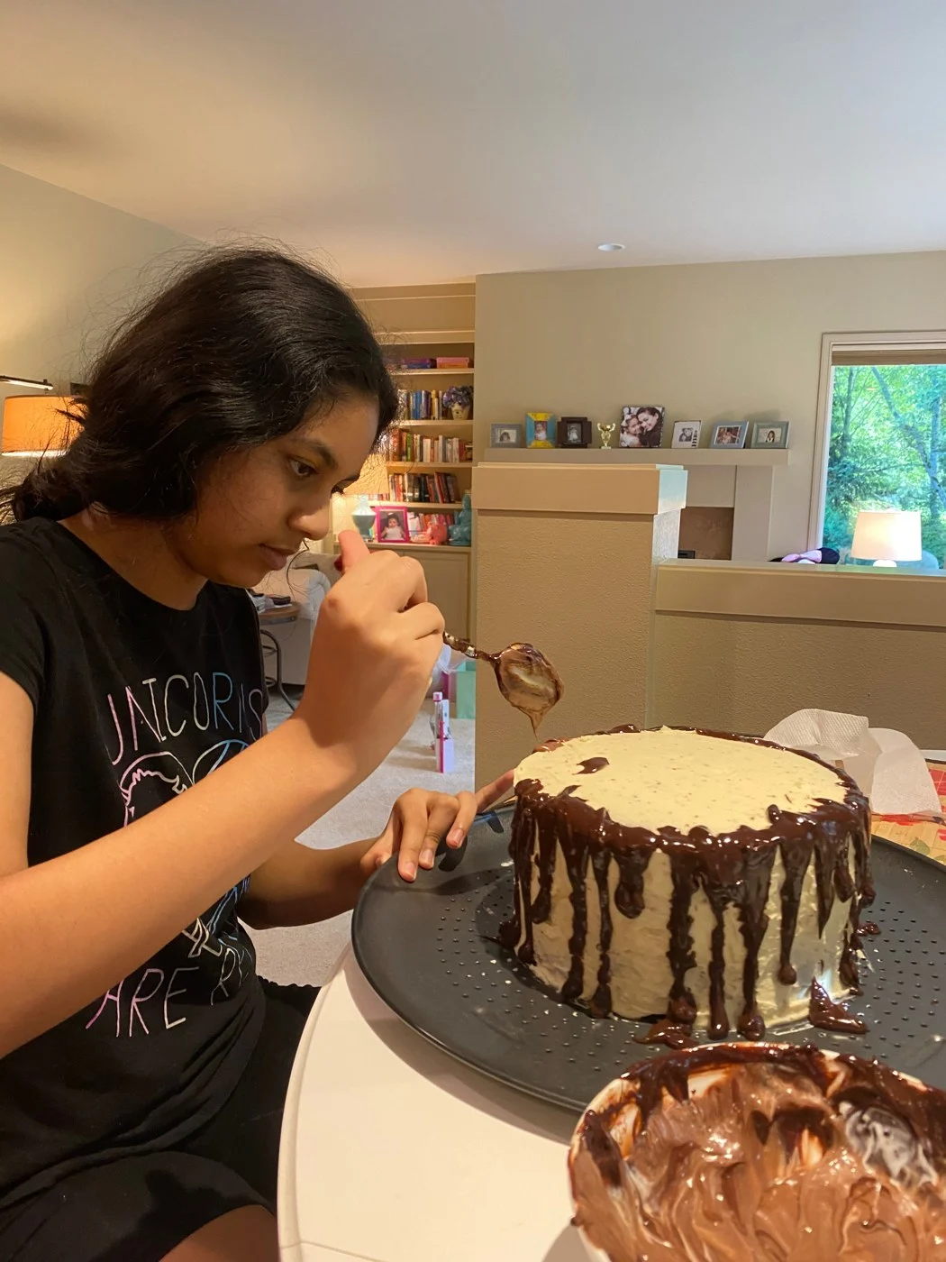Spooning chocolate along the edge of a pale-frosted round cake.