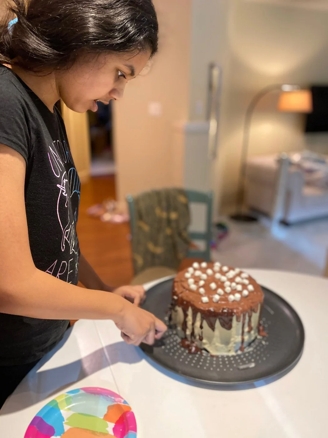 A baker beside a fully decorated marshmallow-topped drip cake.