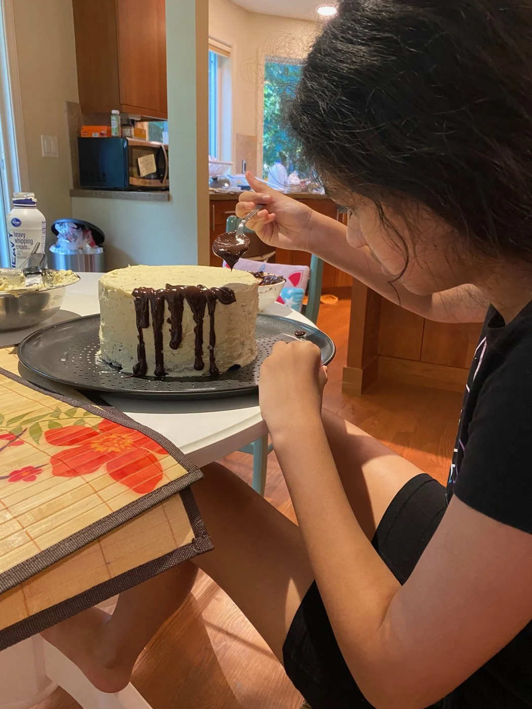 A close side view of spooning chocolate down a cake's frosted sides.