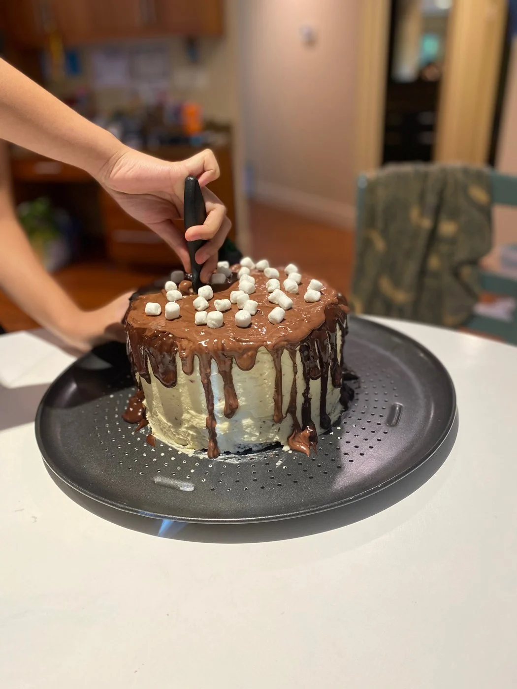 Cutting into a finished marshmallow-topped chocolate-drip cake.
