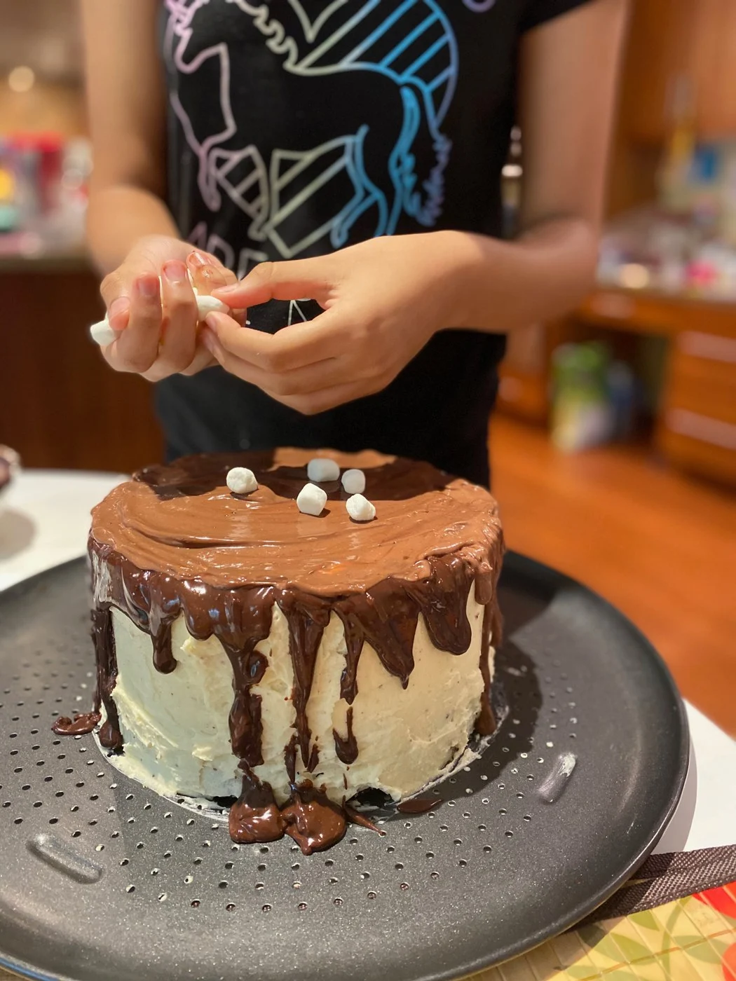 Breaking apart marshmallows to place on top of a chocolate-drip cake.