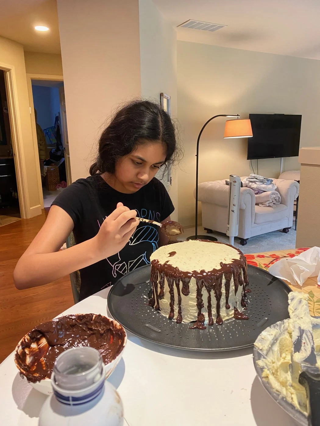Decorating a pale-frosted cake with chocolate sauce and a spoon.