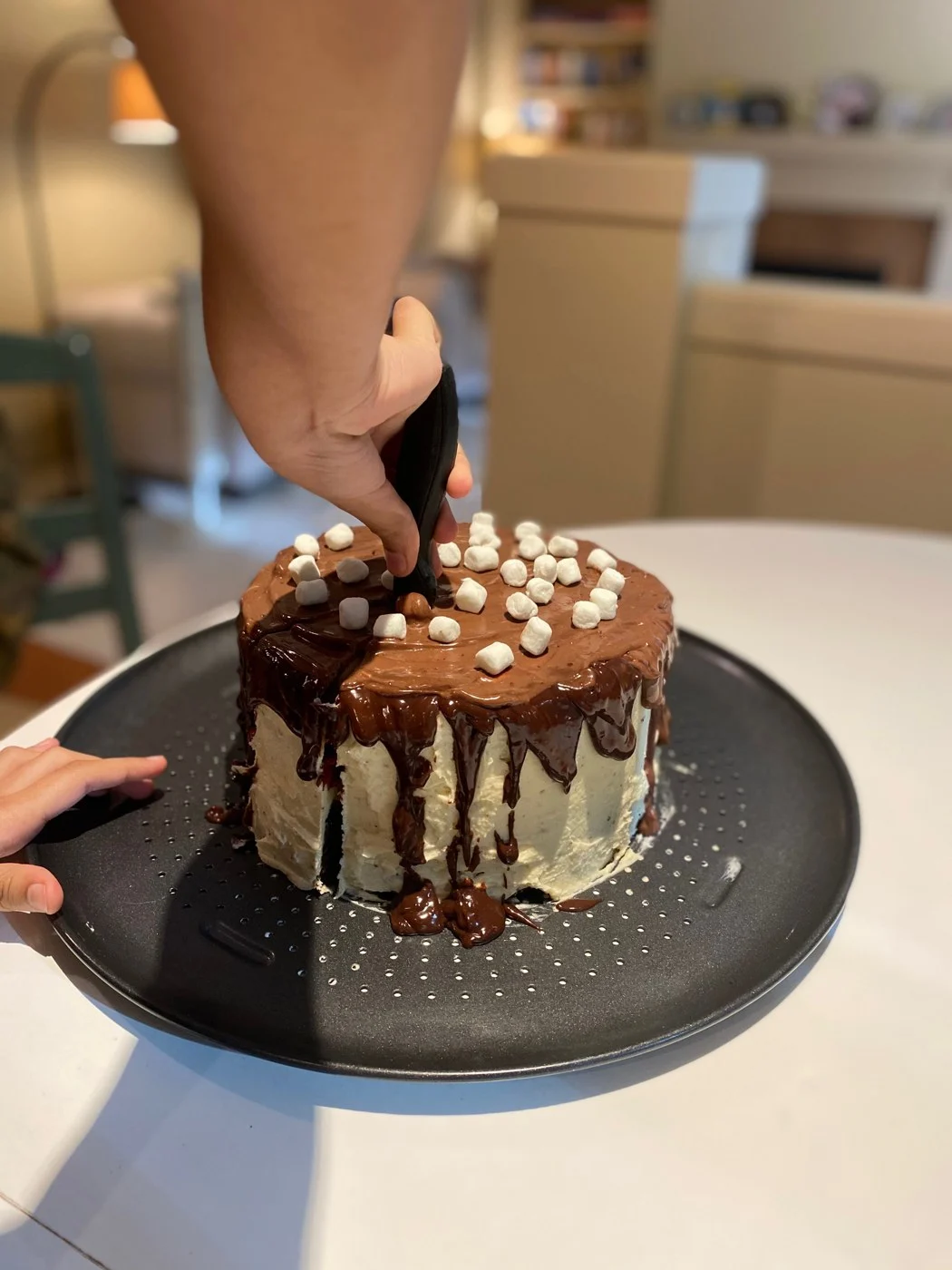 A knife cutting through the marshmallow topping of a chocolate-drip cake.