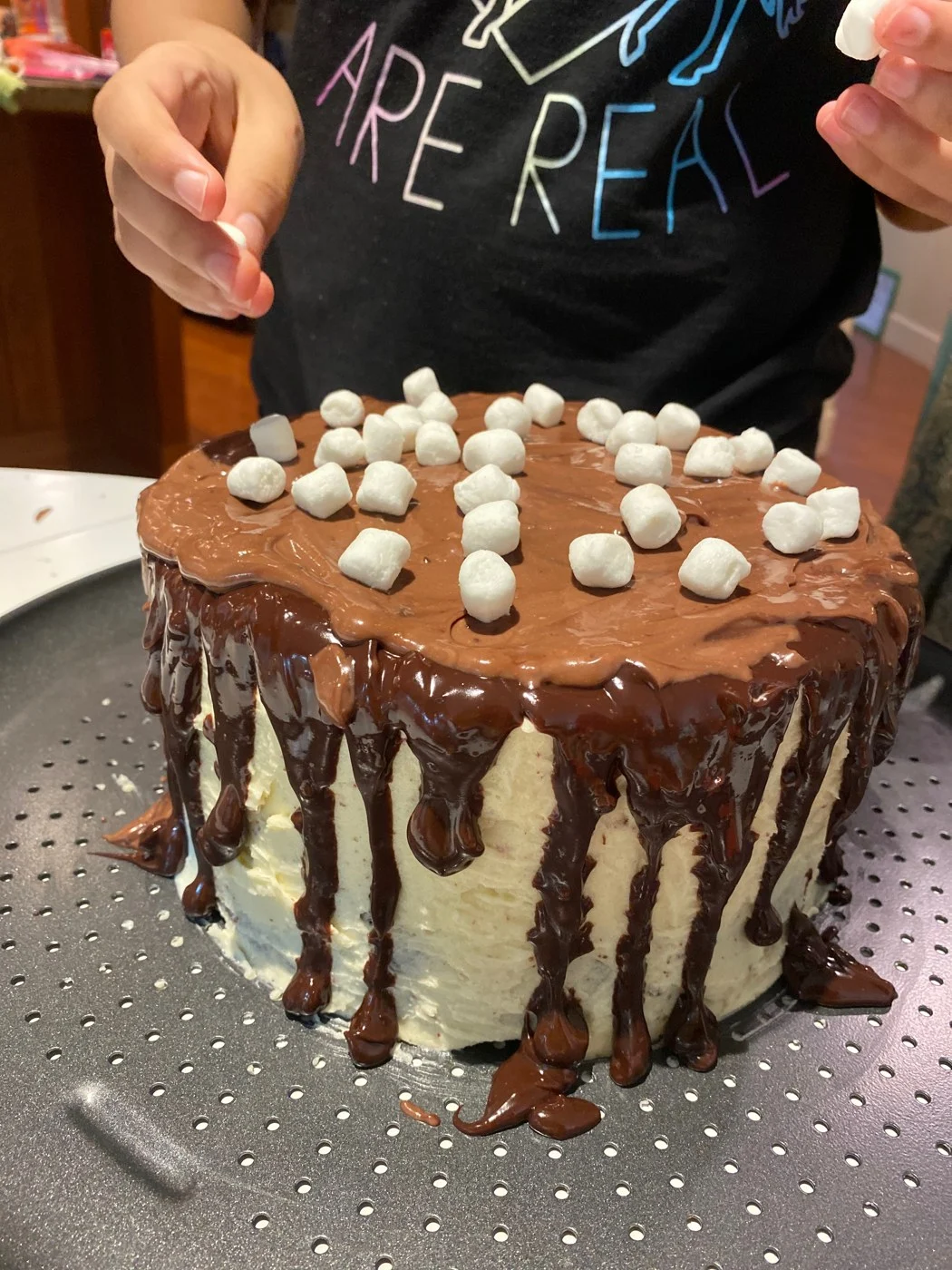 Sprinkling small marshmallows over a chocolate-drip cake.