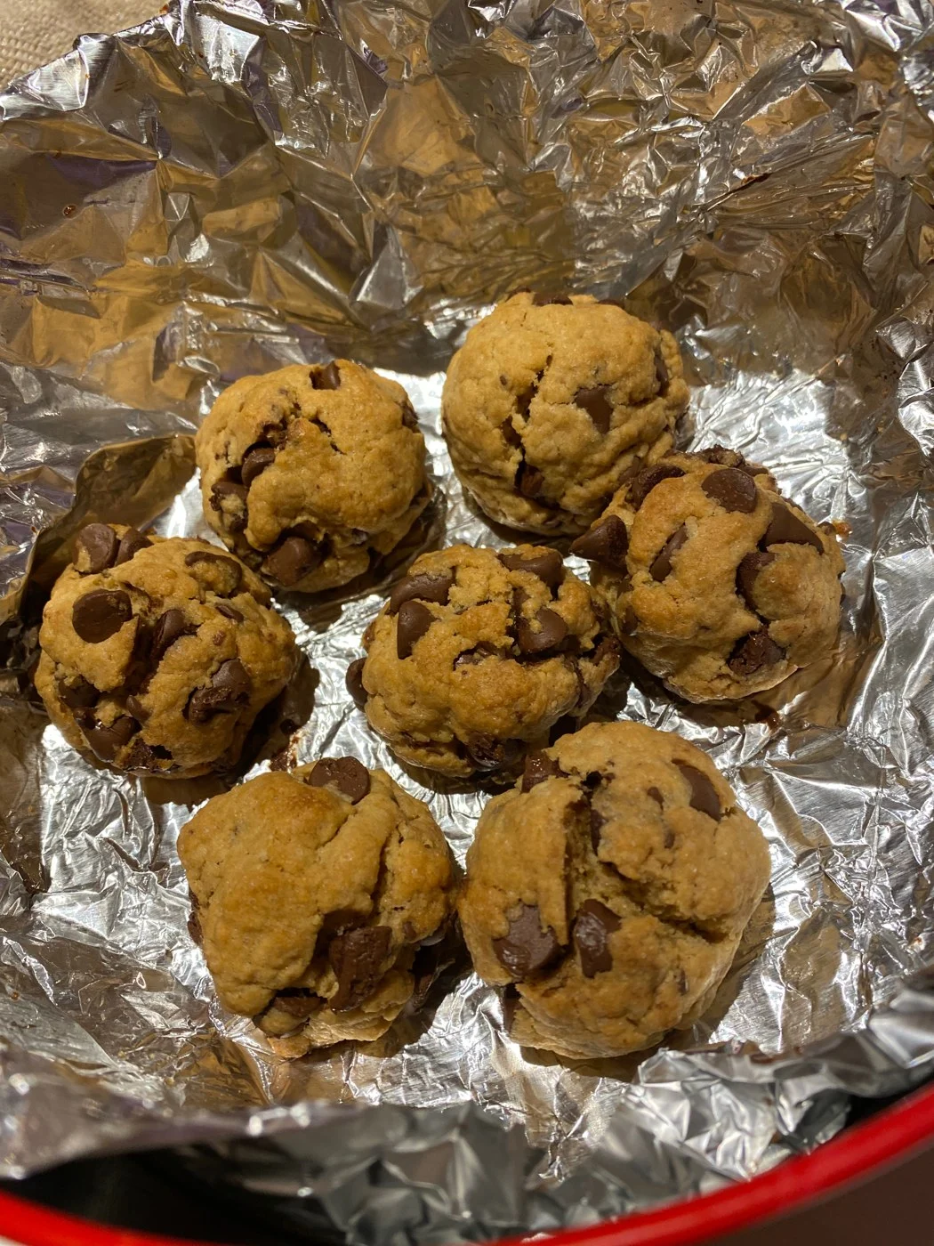 Seven thick chocolate-chip cookies cooling on crinkled foil.