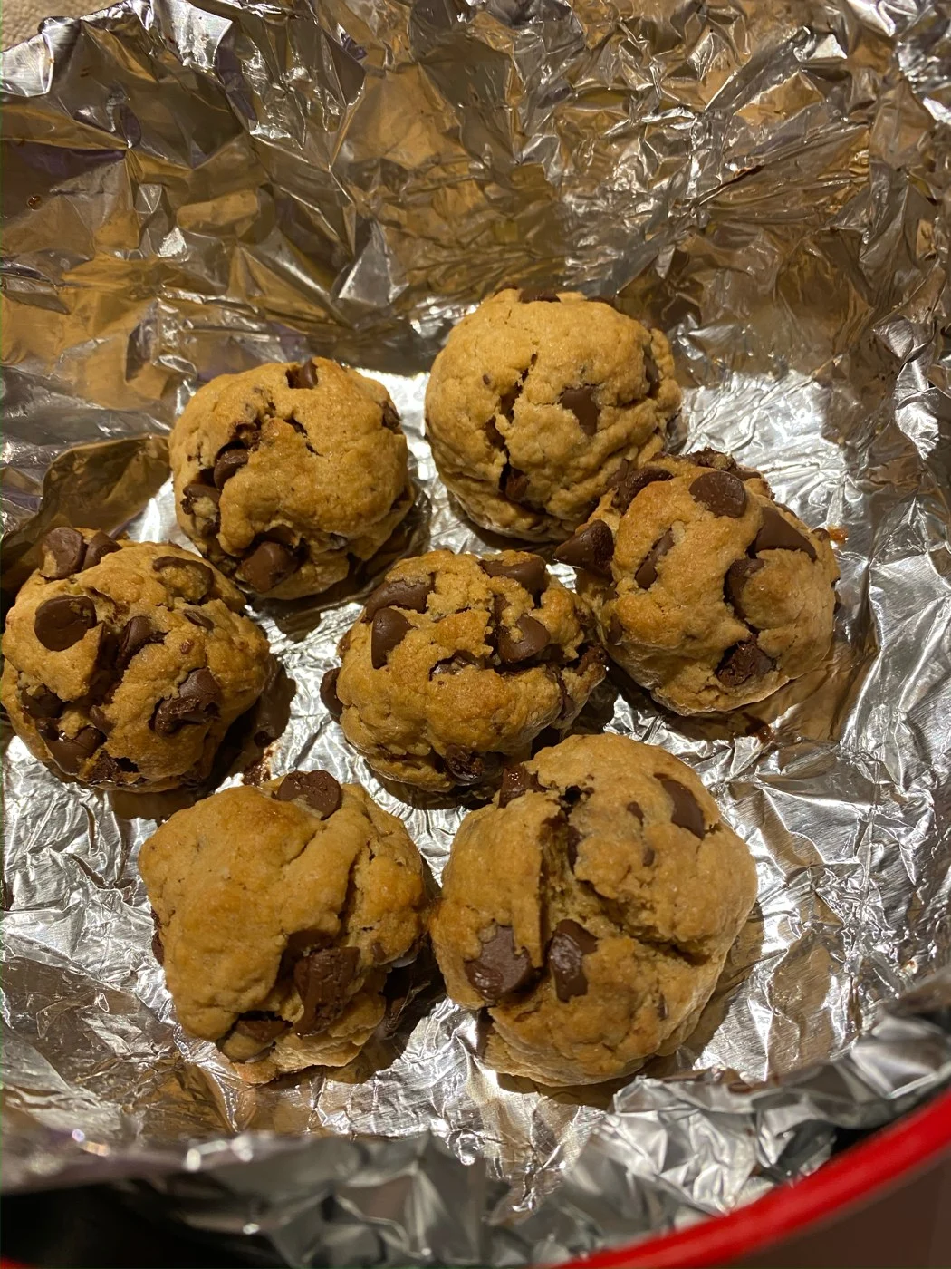 Thick chocolate-chip cookies grouped together on a foil-lined round tray.