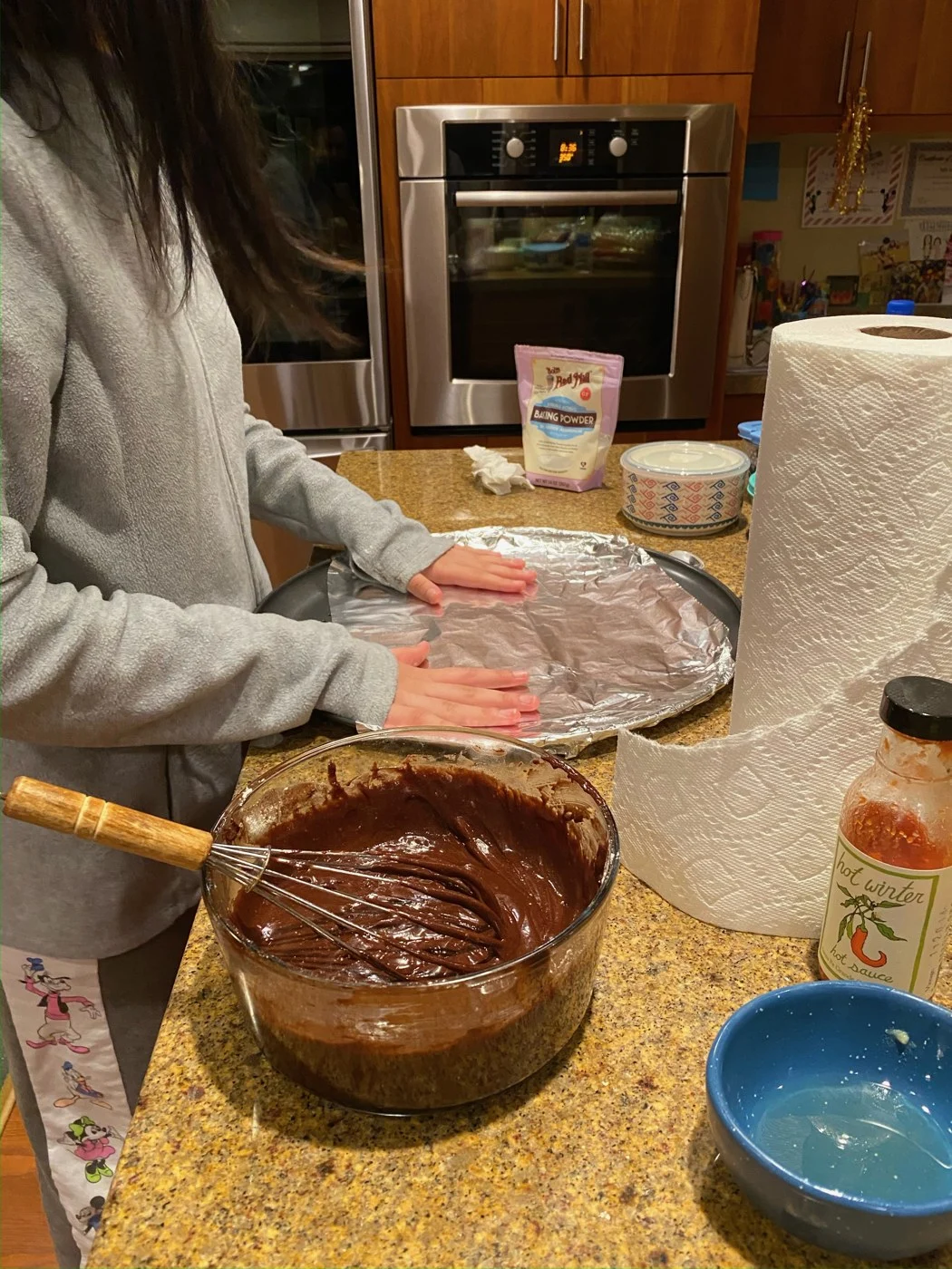 Lining a round baking tray with foil beside chocolate batter and a whisk.