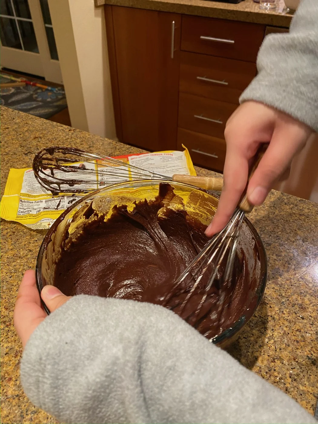 A close view of whisking thick chocolate batter in a glass mixing bowl.