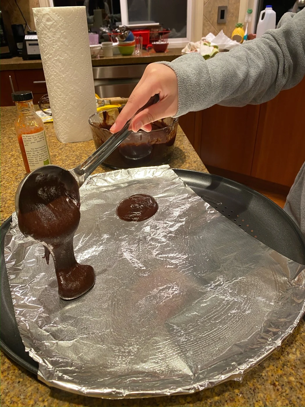 Pouring rounds of chocolate batter onto a foil-lined tray with a ladle.