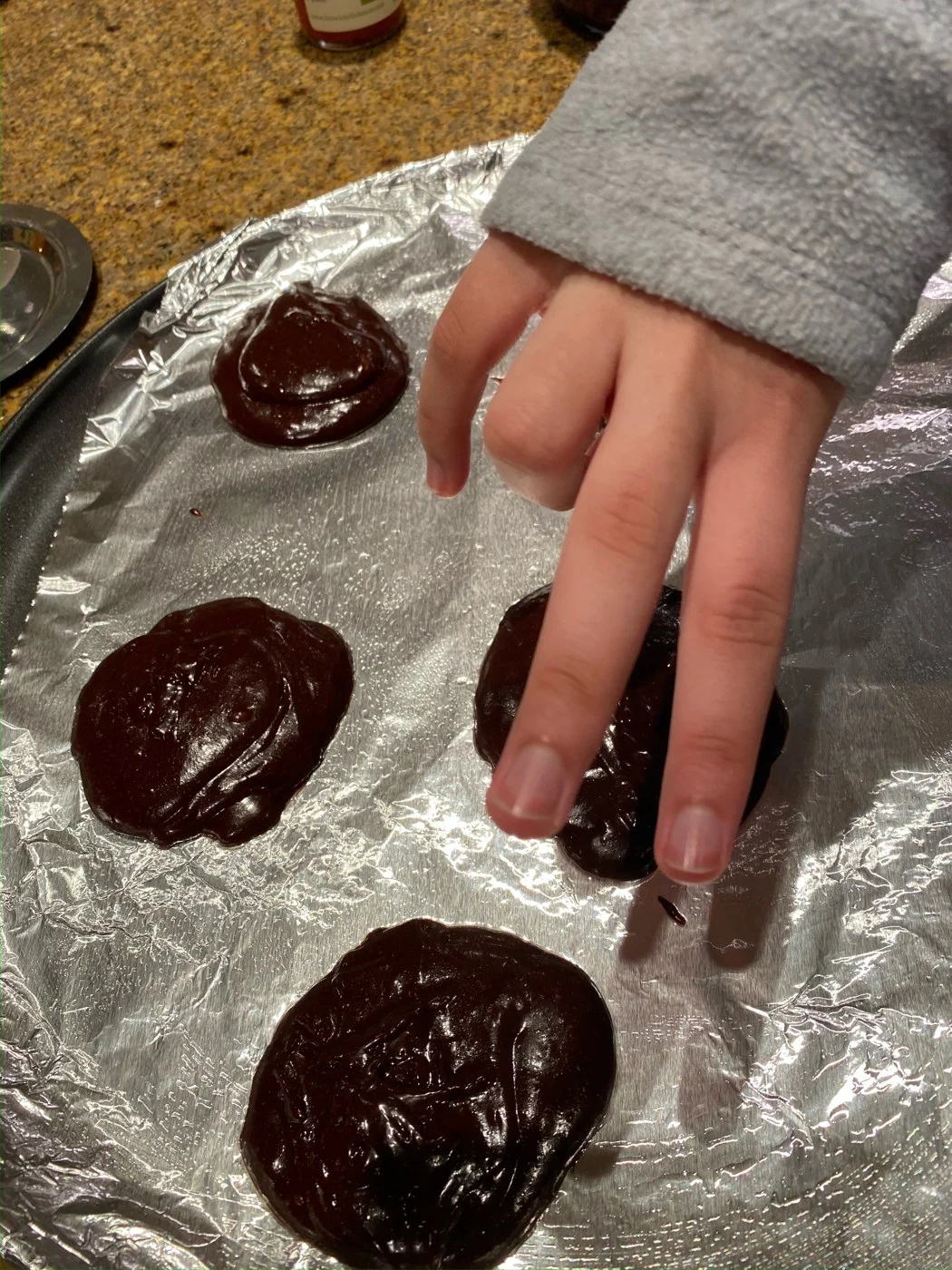 Shaping small rounds of dark cookie batter on a foil-lined baking tray.