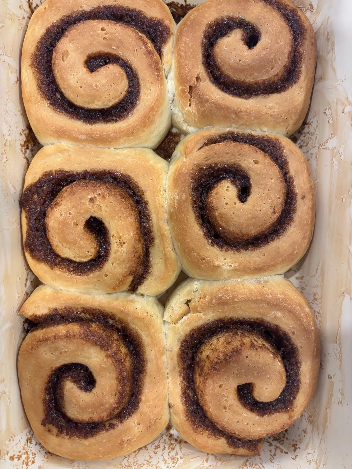 Six large unglazed swirled rolls in a rectangular dish.