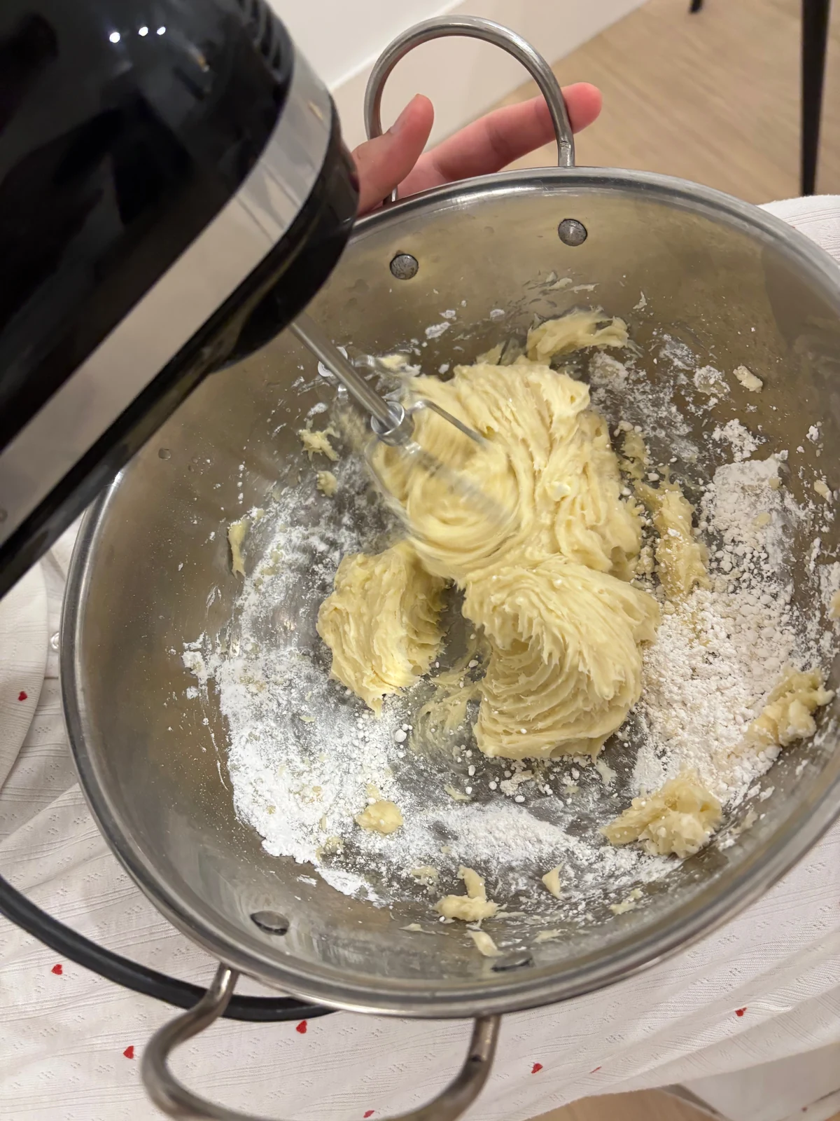 Pale frosting and powdered sugar being mixed in a stainless steel bowl.