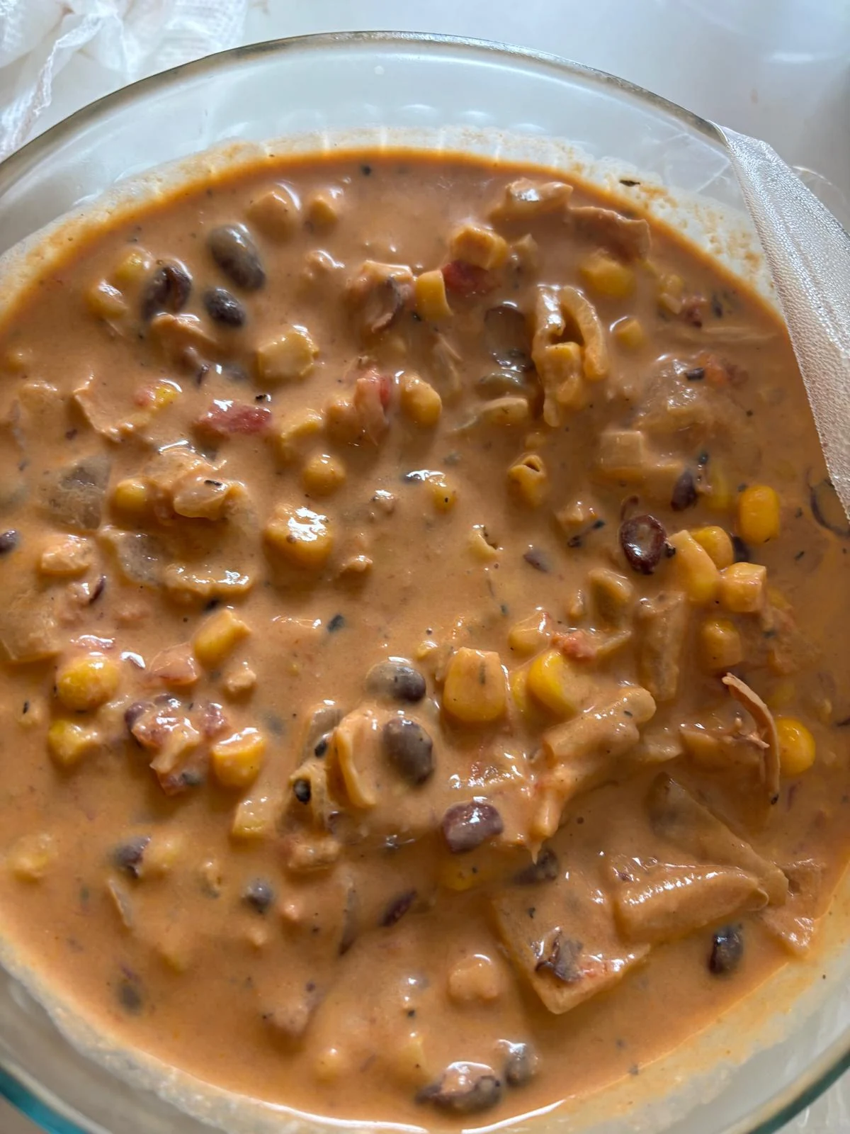 Orange-tan creamy soup with corn, black beans, tomato pieces and pale chunks/strands resembling shredded chicken; some wider softened strips.