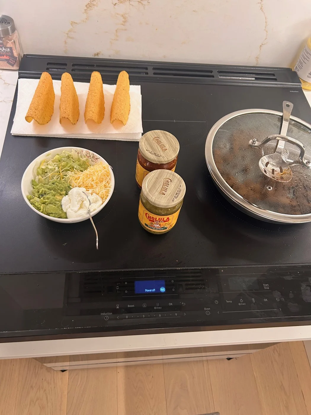 Four empty taco shells arranged above toppings on the stovetop.