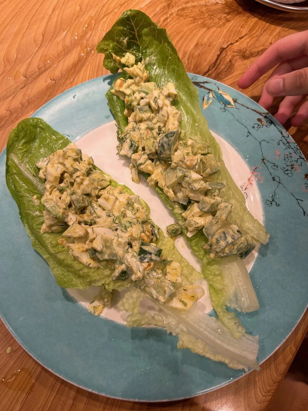Two long lettuce leaves filled with a pale chunky salad on a blue plate.
