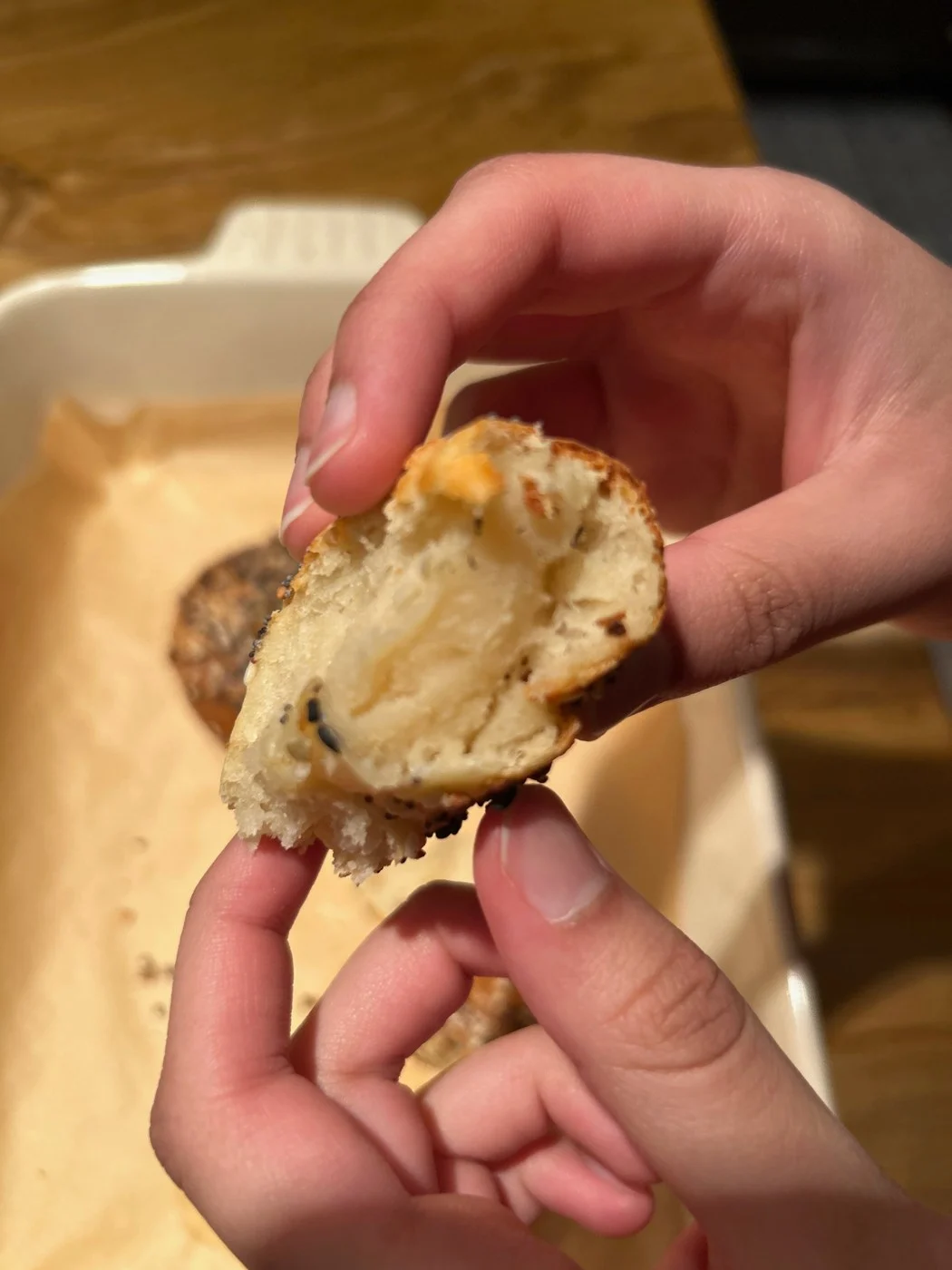 Hands holding open a seeded bread bite to show its creamy center.