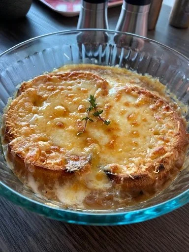 A bowl of soup topped with toasted bread, browned melted cheese and a sprig of herb.