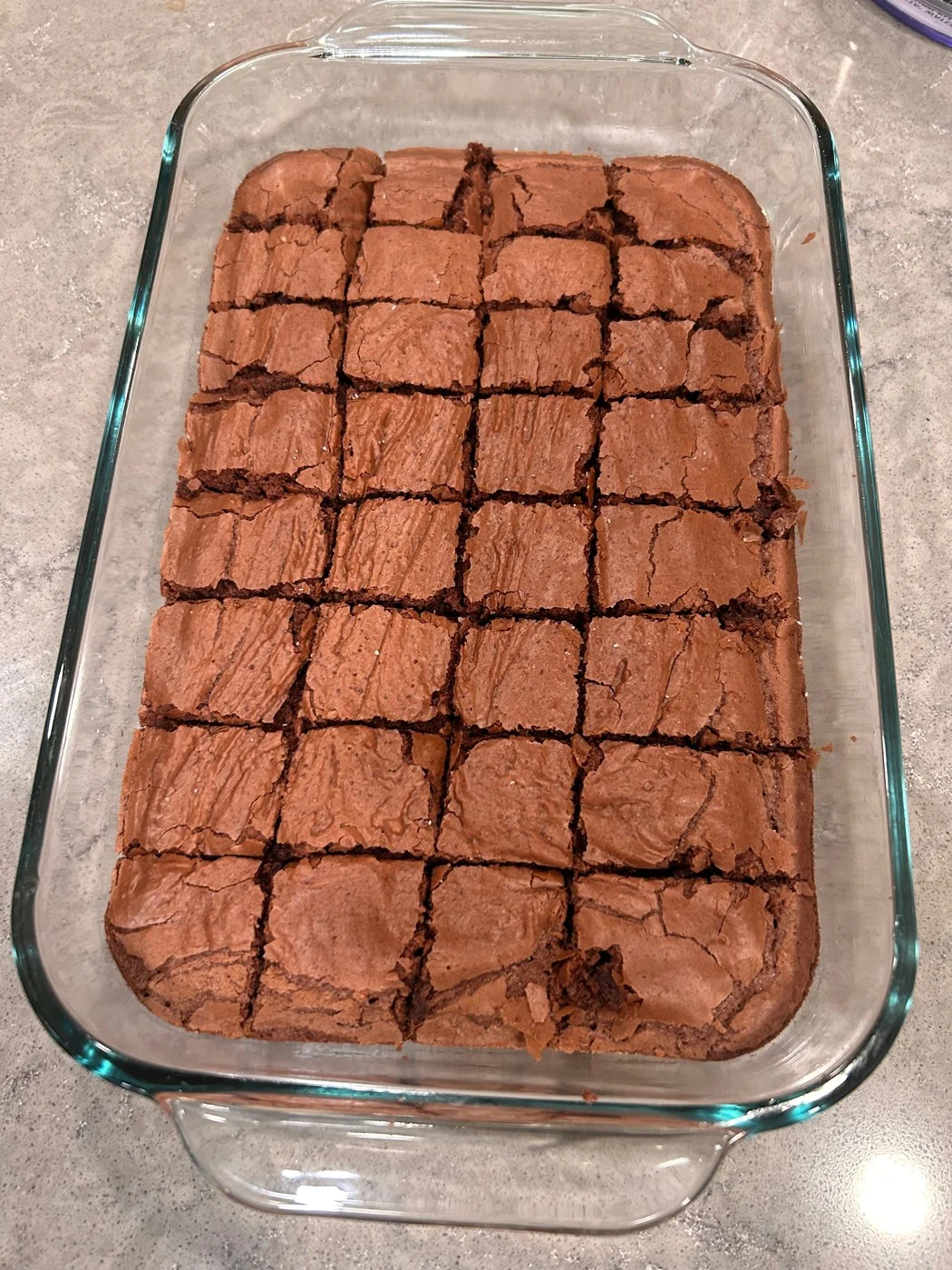 A baked brownie slab scored into small squares in its glass dish.