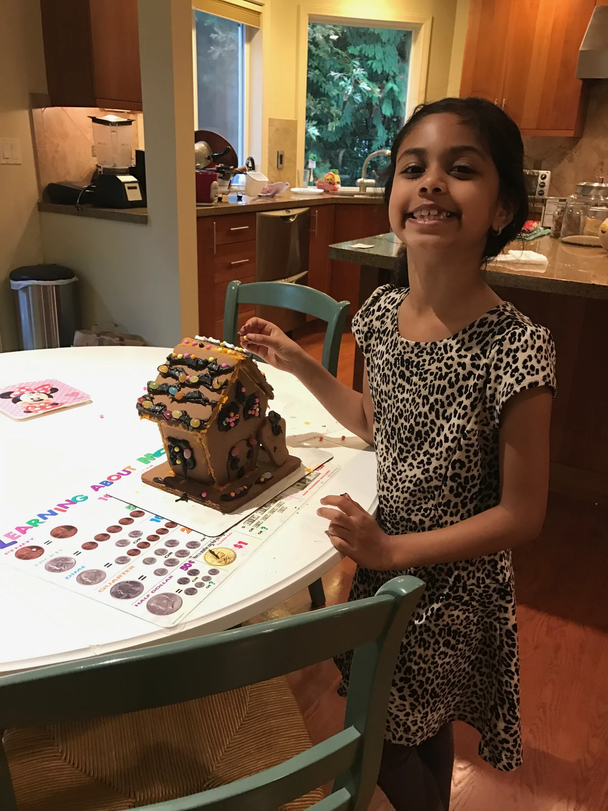 Person with small assembled brown cookie house, candy and icing decorations.