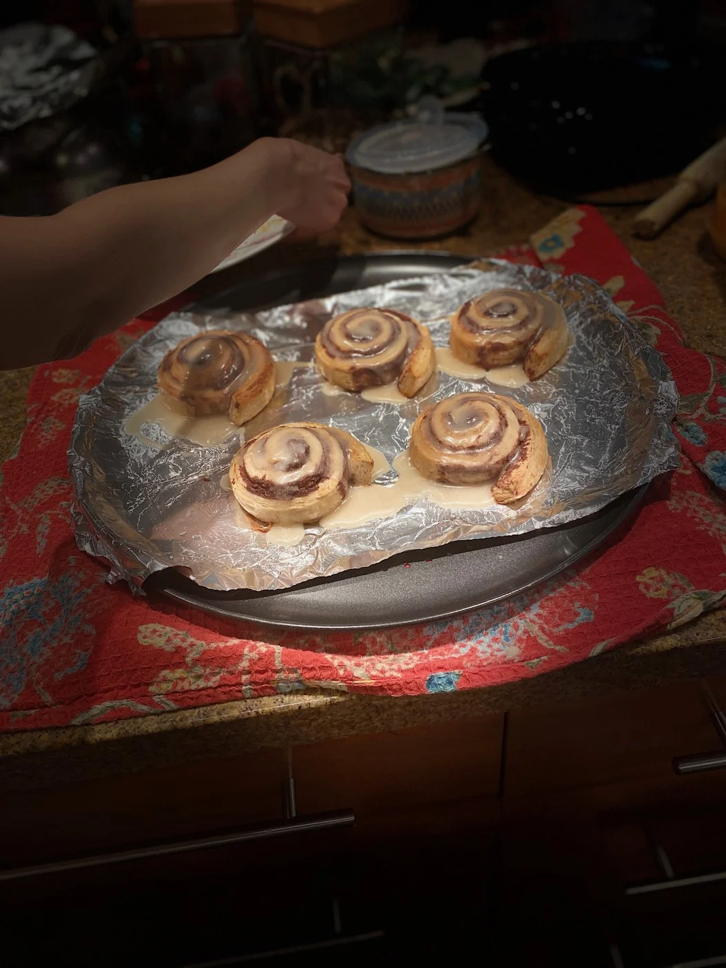Five glazed cinnamon swirls resting on a foil-lined tray.
