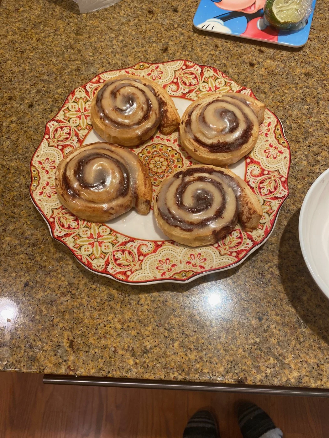 Four glazed cinnamon swirls on a red-and-cream patterned plate.