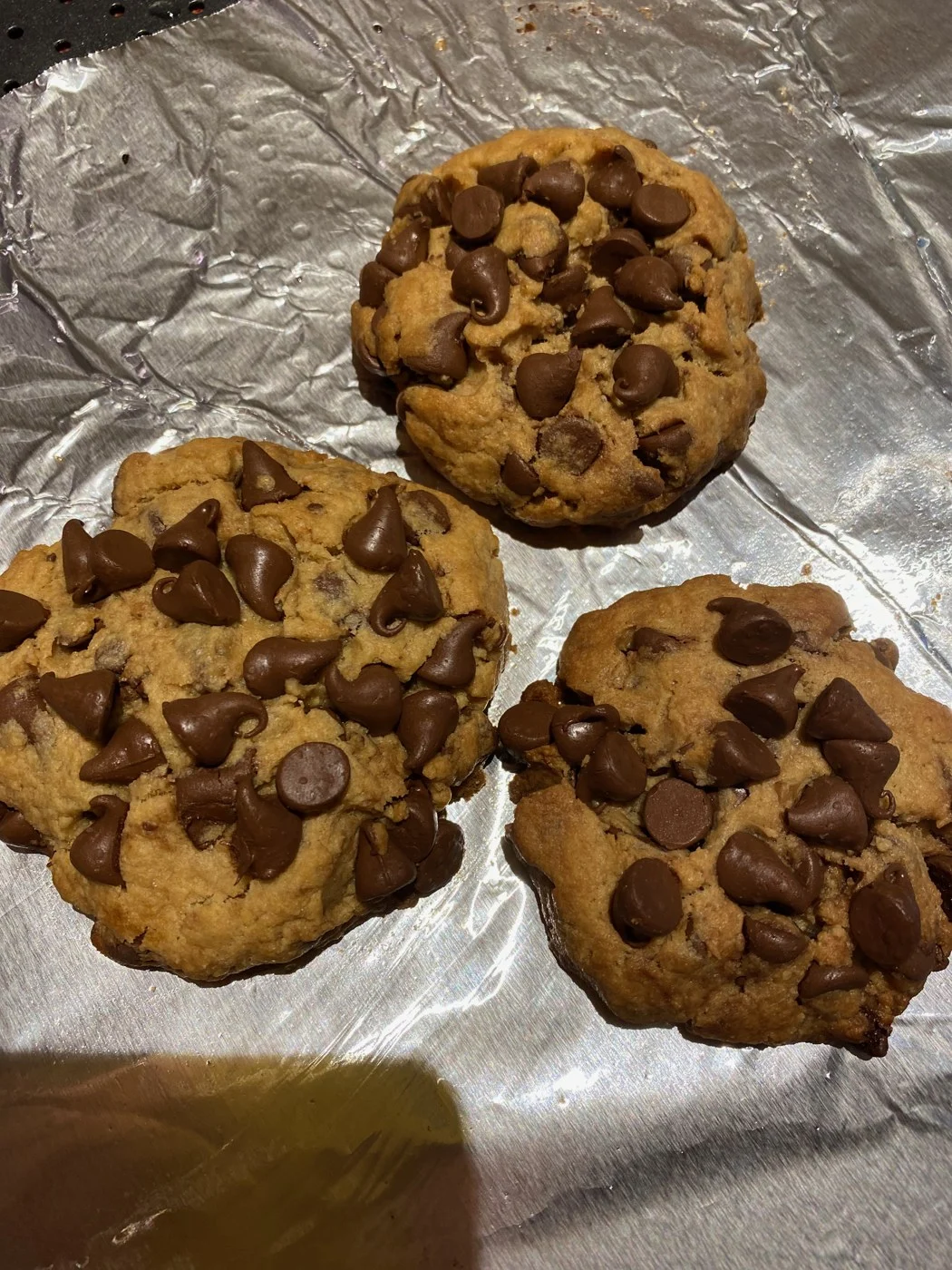Three golden cookies with abundant chocolate chips on their surfaces.