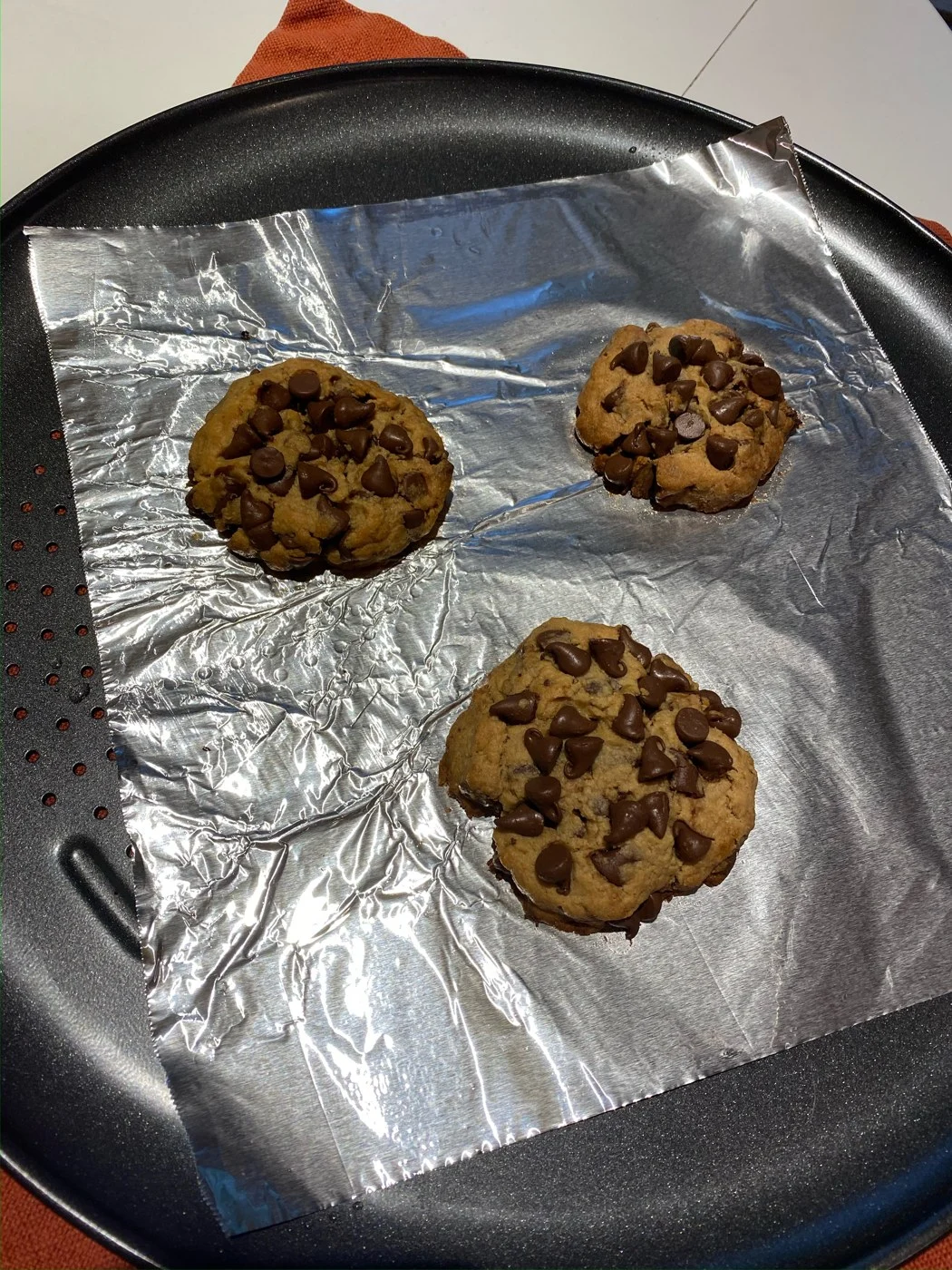 Three chocolate-chip cookies on a round foil-lined tray.