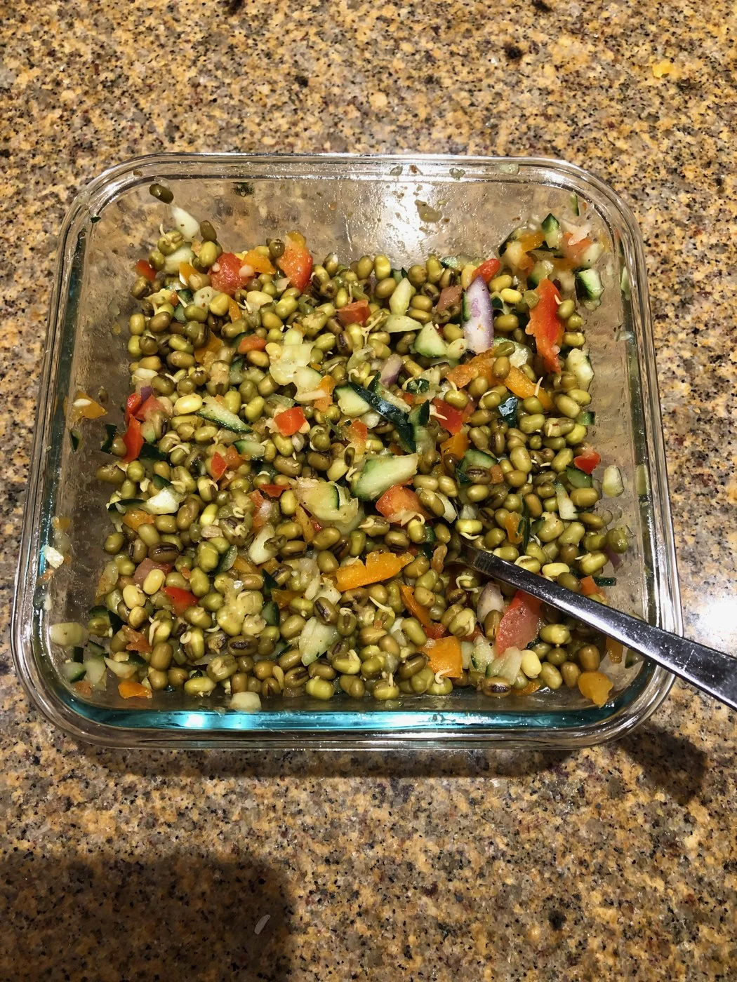 Whole green legumes mixed with chopped vegetables in a glass dish with a serving spoon.