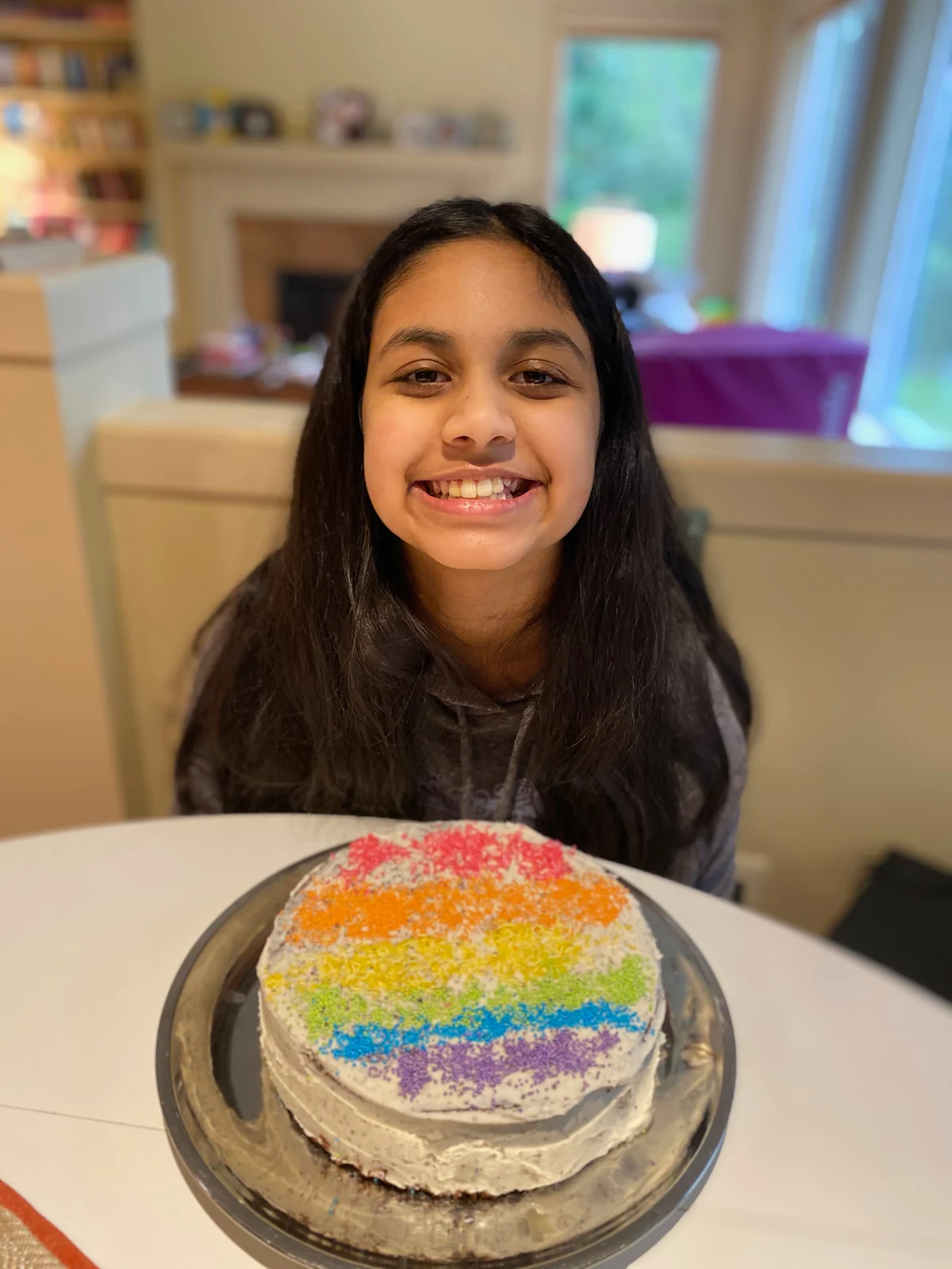 Person behind the same small pale-frosted rainbow-stripe cake as 003.