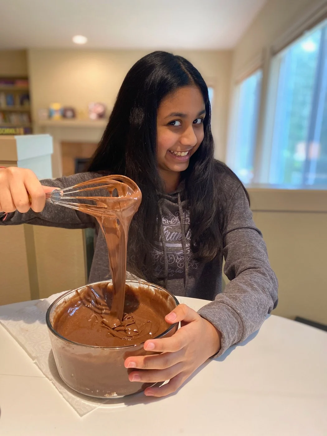 Lifting a whisk to show chocolate batter falling into a glass bowl.