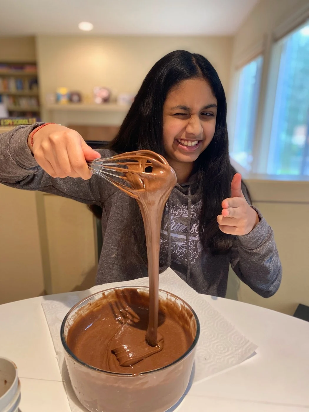 A baker giving a thumbs-up while lifting a chocolate-covered whisk.