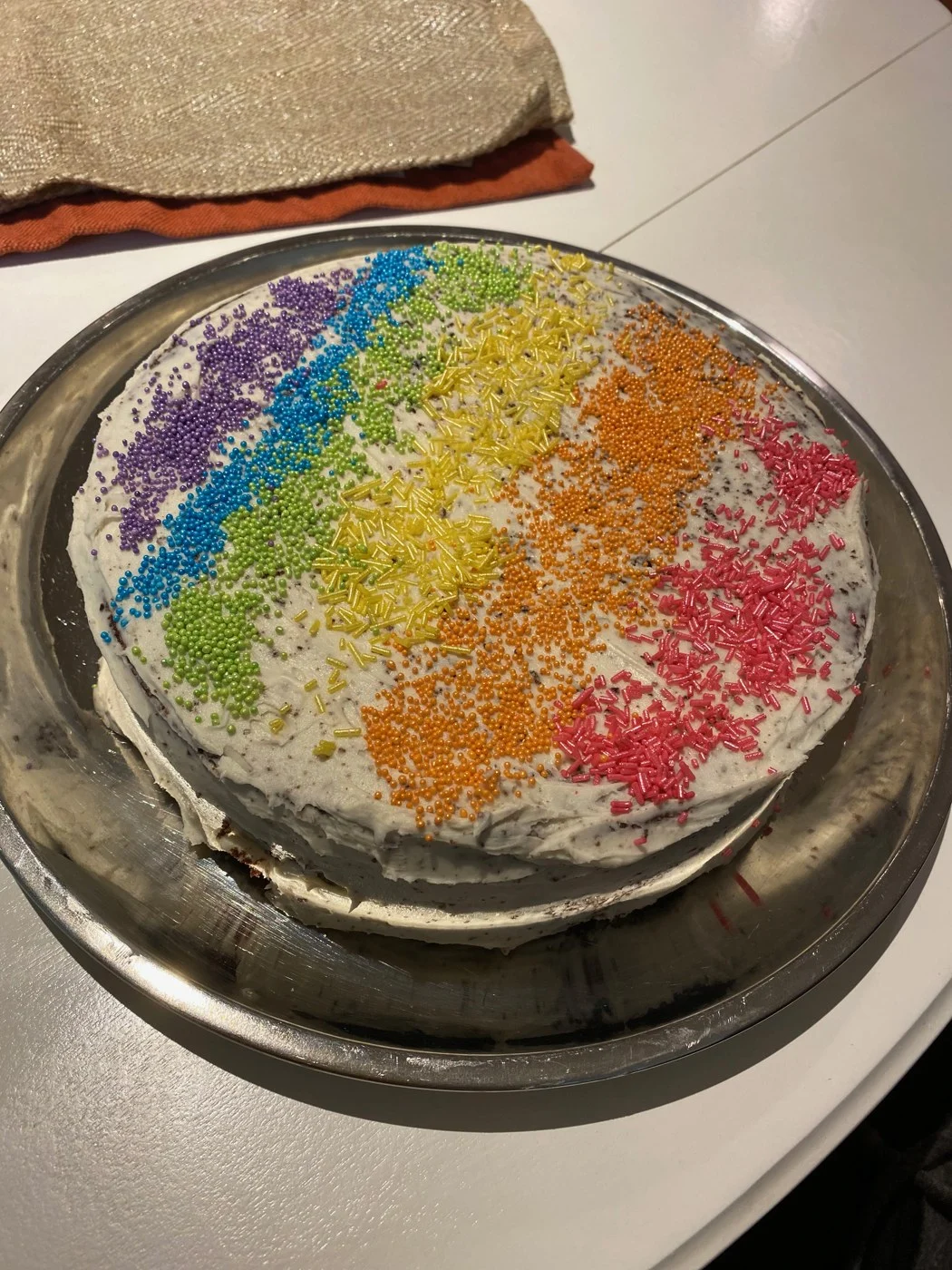 An overhead view of a pale-frosted cake with rainbow sprinkle stripes.