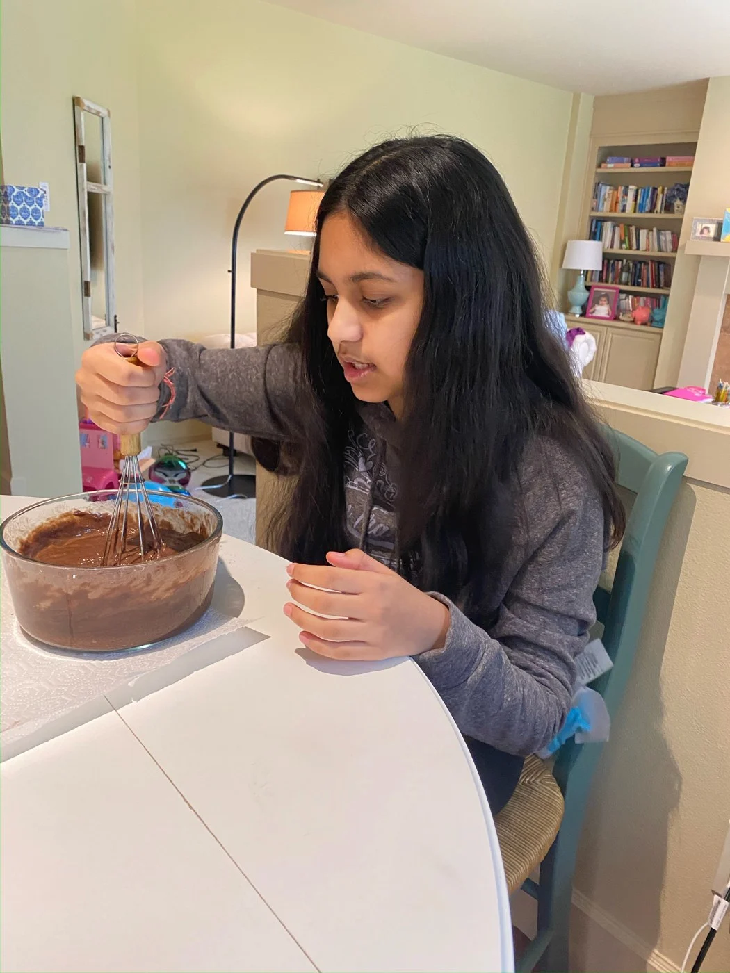 A baker whisking chocolate batter while seated at the dining table.
